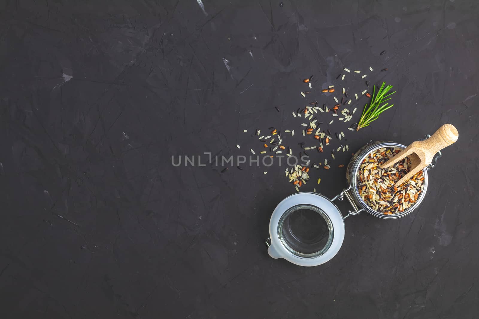 Black, purple, and white rice (Oryza sativa) mix in glass jar on black stone concrete textured surface background. Top view with copy space for your text.