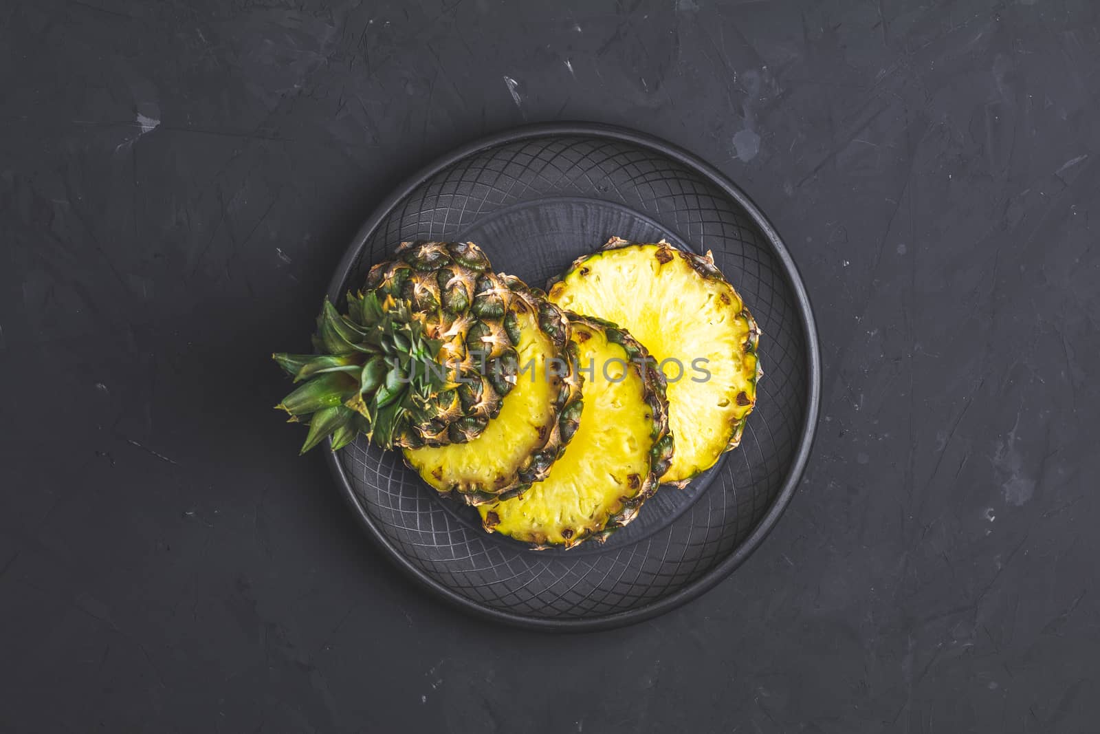 Sliced pineapple in ceramic plate on black concrete surface by ArtSvitlyna