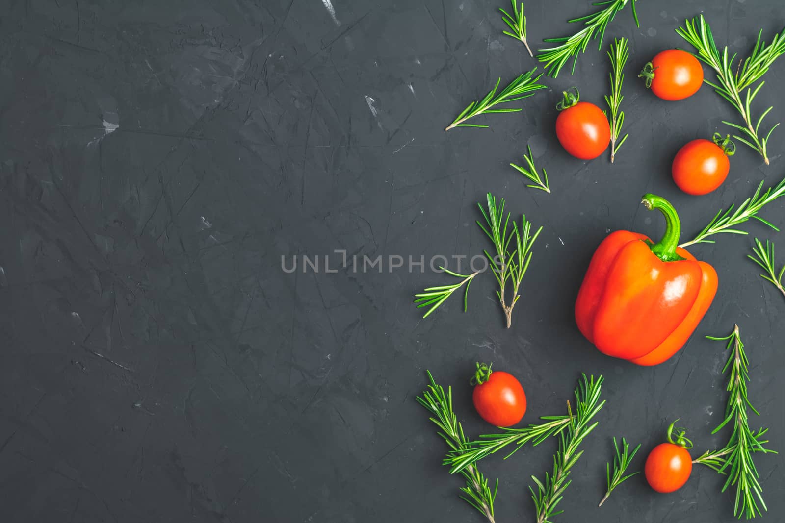 Rosemary bunch, raw pepper and cherry tomatoes on black stone concrete textured surface background. Top view with copy space for your text.