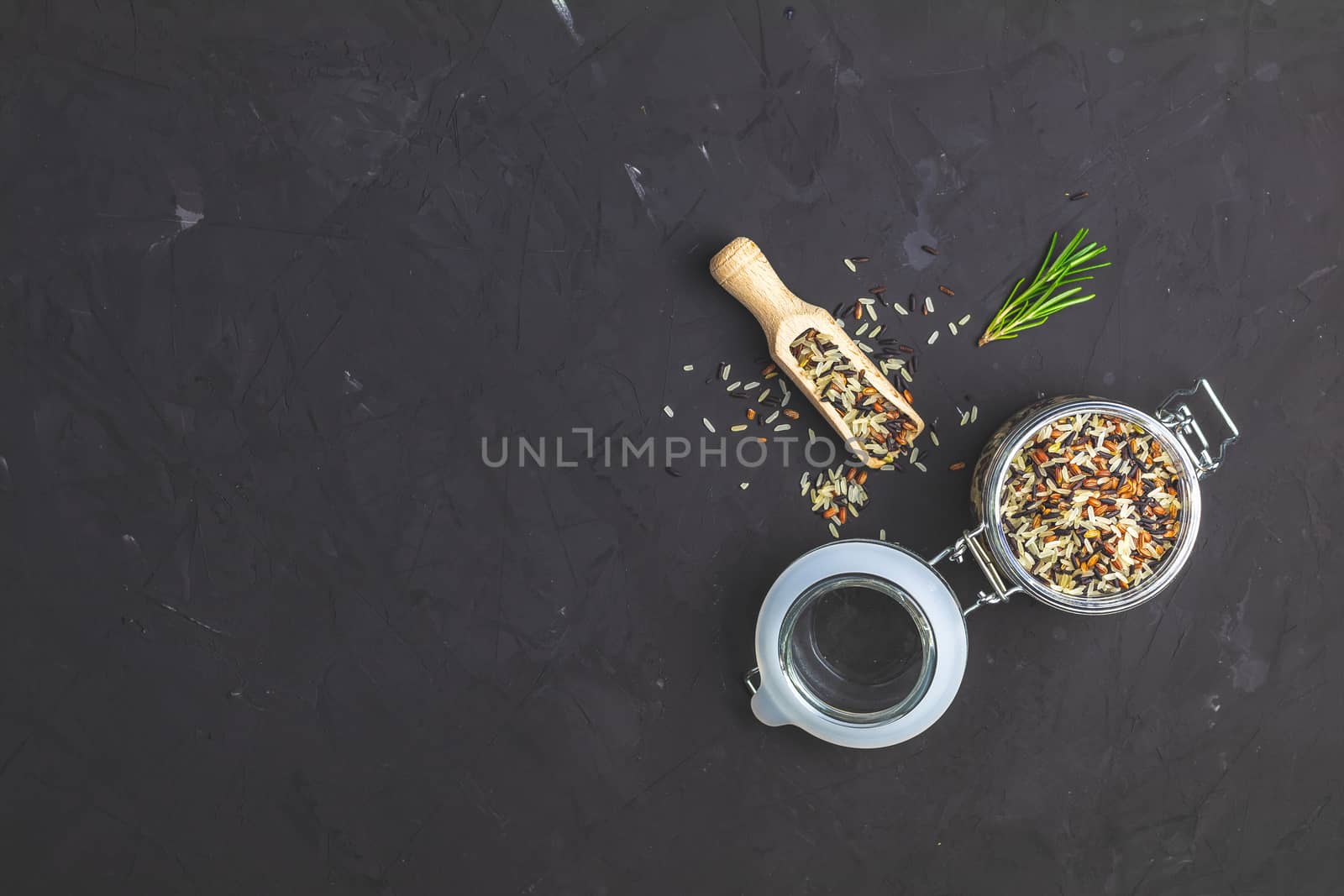 Black, purple, and white rice (Oryza sativa) mix in glass jar on black stone concrete textured surface background. Top view with copy space for your text.