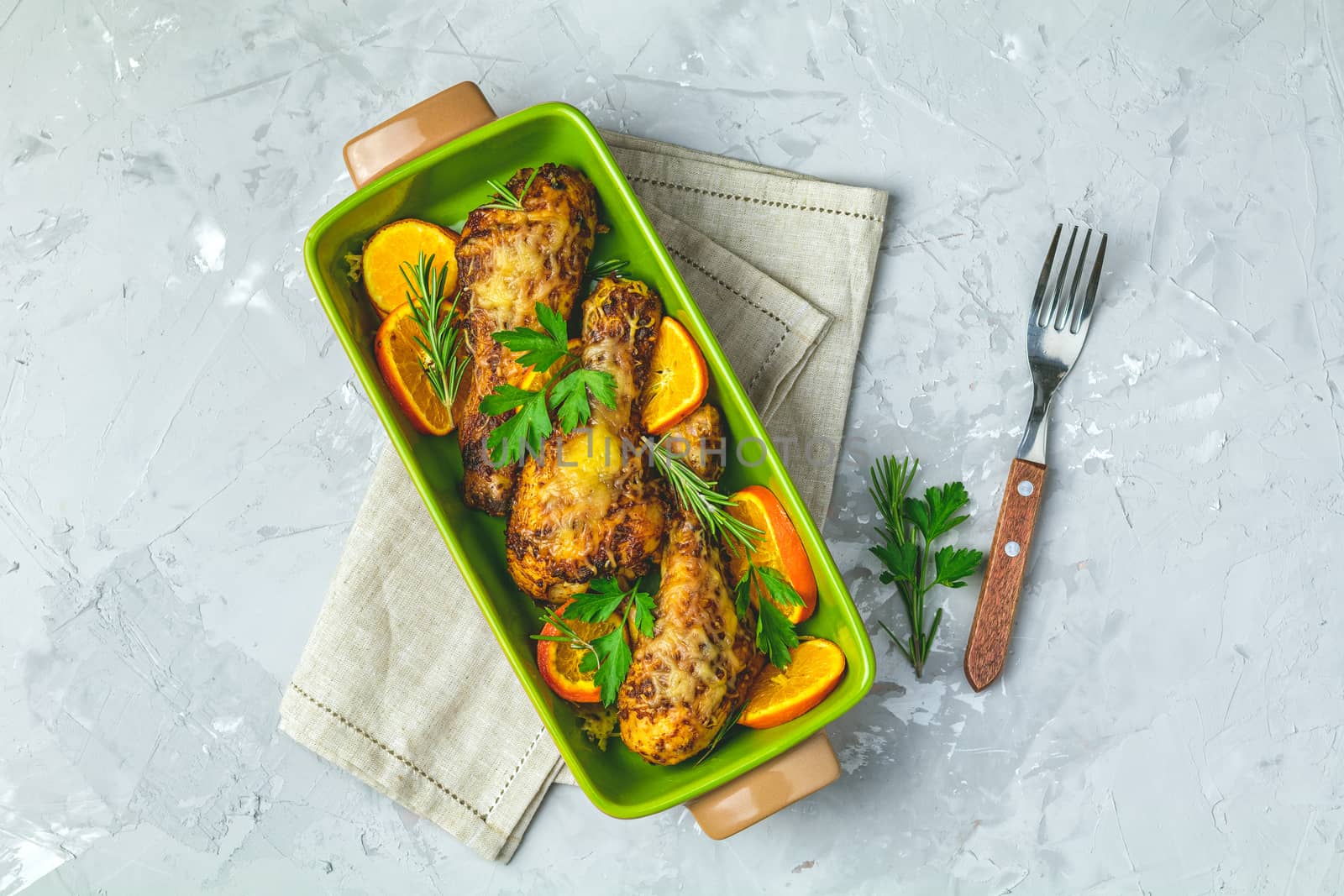 Baked chicken drumstick in a green dish with orange and rosemary by ArtSvitlyna