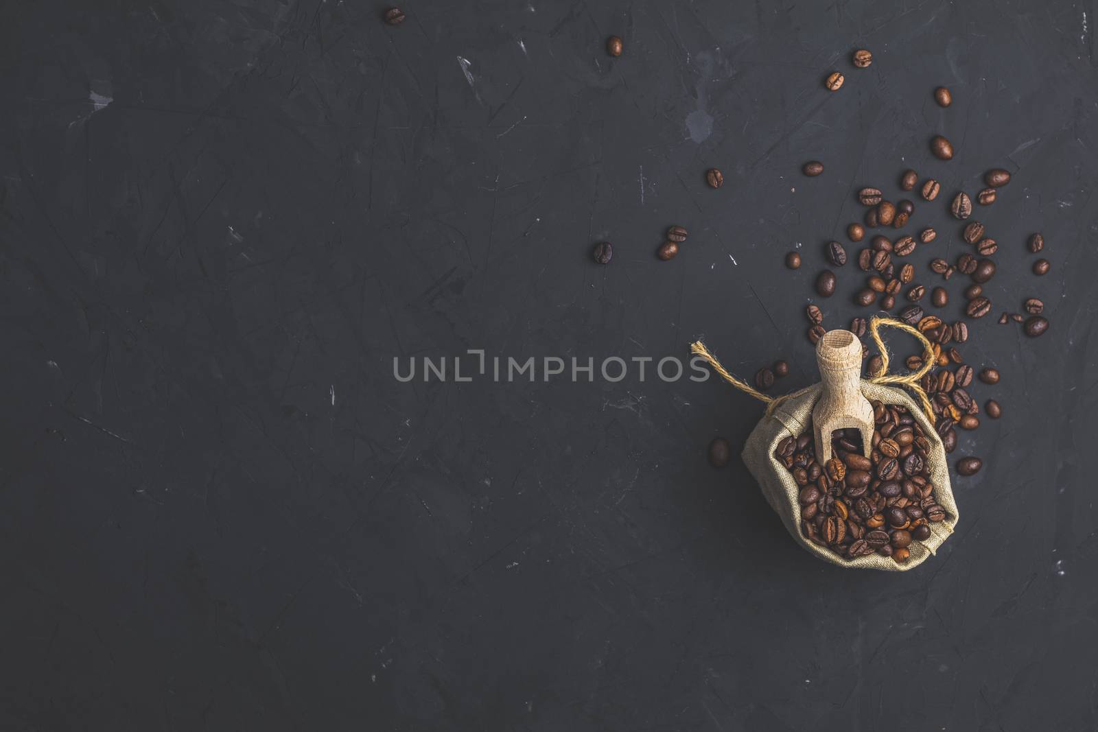 Purse with roasted beans and wooden scoop on black stone concrete textured surface background. Top view with copy space for your text.