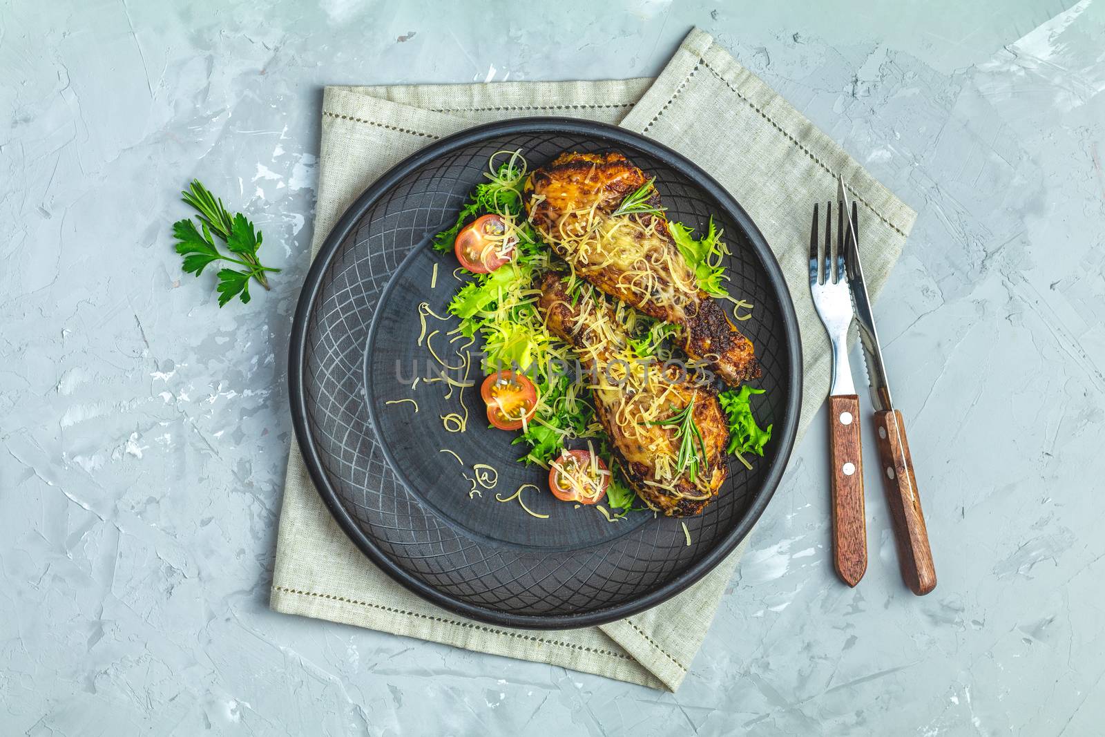 Baked chicken drumstick in a black ceramic plate with orange and rosemary, light gray stone concrete surface, top view, copy space.