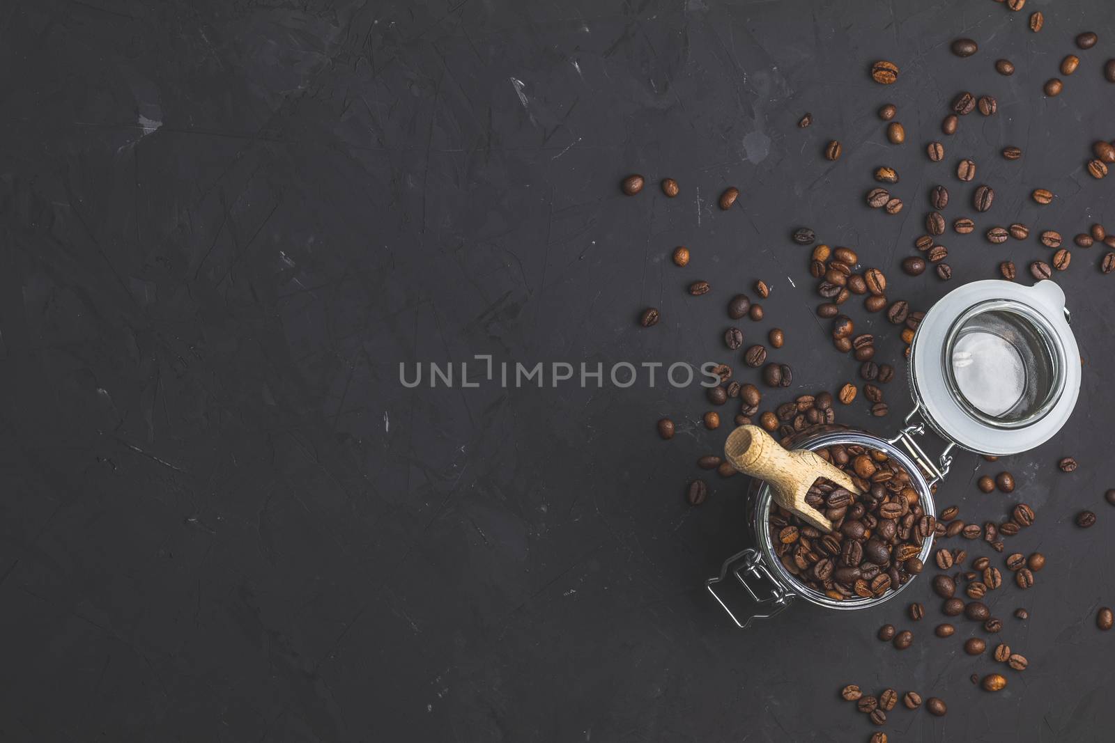 Glass jar with roasted beans and wooden scoop on black stone concrete textured surface background. Top view with copy space for your text.