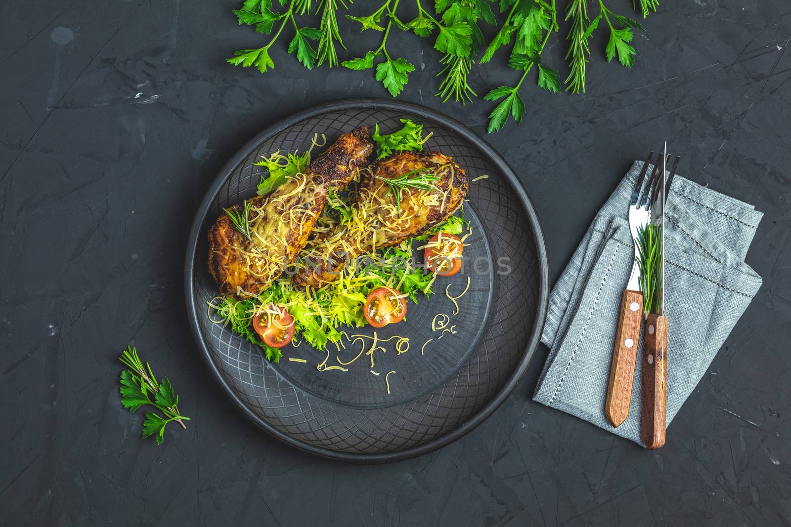 Baked chicken drumstick in a black ceramic plate with orange and rosemary, black stone concrete surface, top view, copy space.