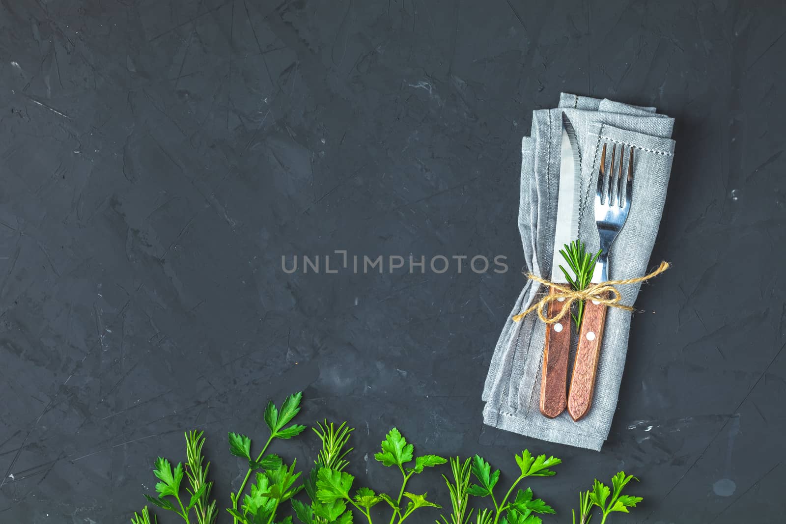 Rustic vintage set of cutlery knife, fork. Black stone concrete surface background, fresh herb decor. Top view, copy space.