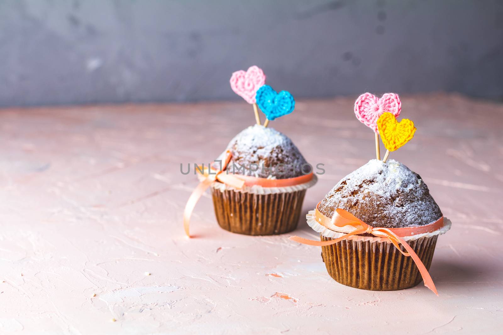 Tasty delicious homemade muffin on light pink living coral stone concrete surface with knitting hearts, copy space. Sweet food for valentines day.