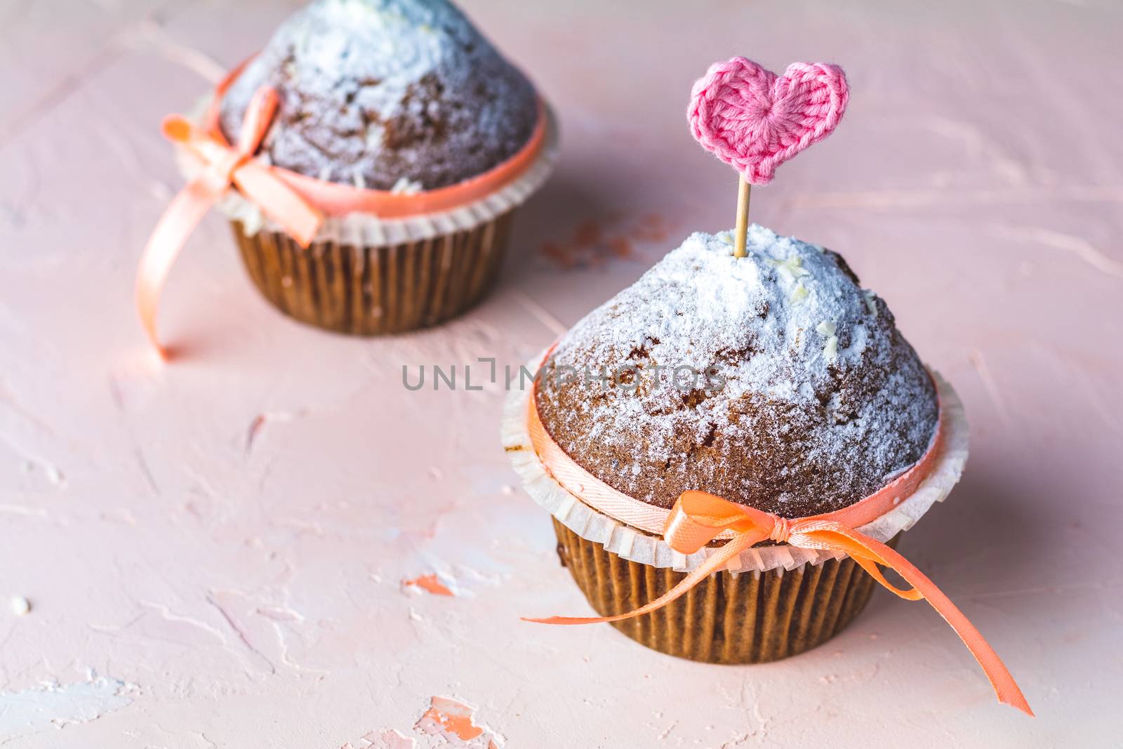 Tasty delicious homemade muffin on light pink living coral stone concrete surface with knitting hearts, copy space. Sweet food for valentines day.