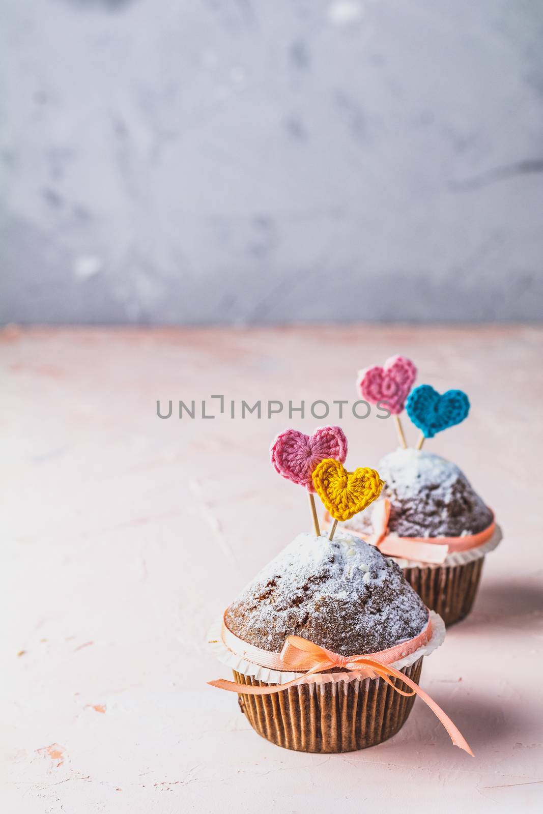 Tasty delicious homemade muffin on light pink living coral stone concrete surface with knitting hearts, copy space. Sweet food, Beautiful food concept for Valentine day or Wedding, Birthday