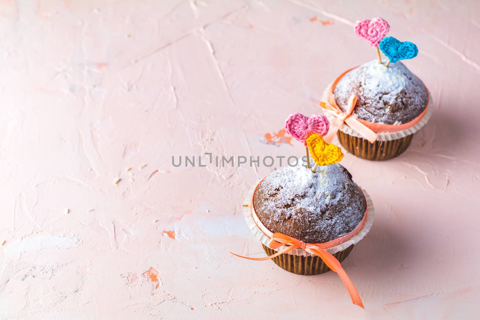 Tasty delicious homemade muffin on light pink living coral stone concrete surface with knitting hearts, copy space. Sweet food for valentines day.