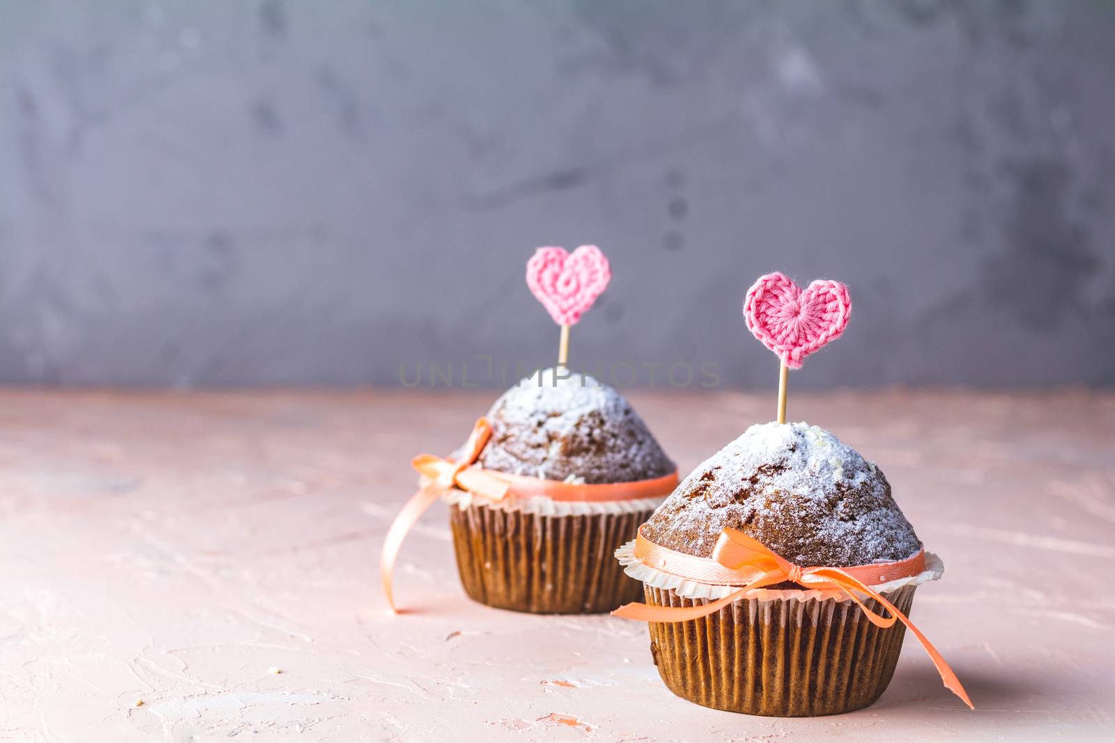 Tasty delicious homemade muffin on light pink living coral stone concrete surface with knitting hearts, copy space. Sweet food for valentines day.