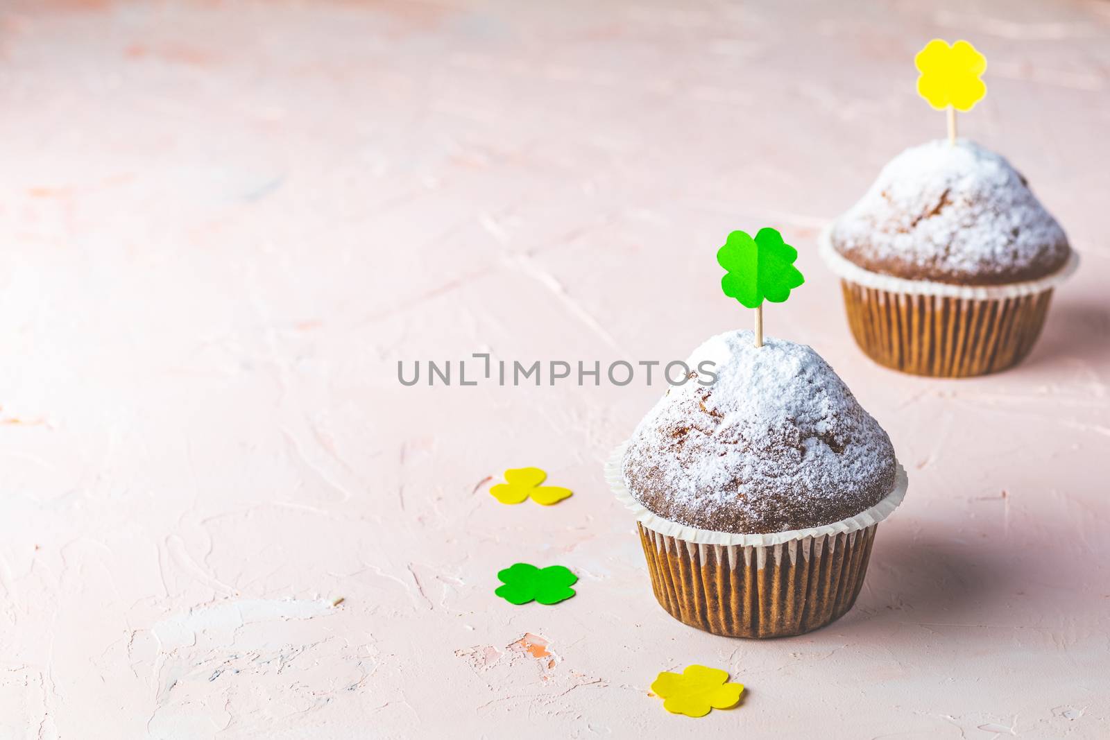 Tasty delicious homemade muffins on light pink living coral stone concrete surface with holiday attributes, copy space. Beautiful sweet food concept for Saint Patrick day.