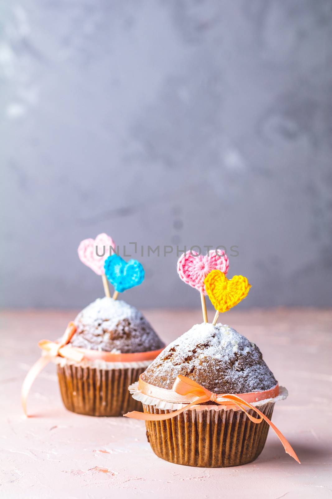 Tasty delicious homemade muffin on light pink living coral stone concrete surface with knitting hearts, copy space. Sweet food for valentines day.