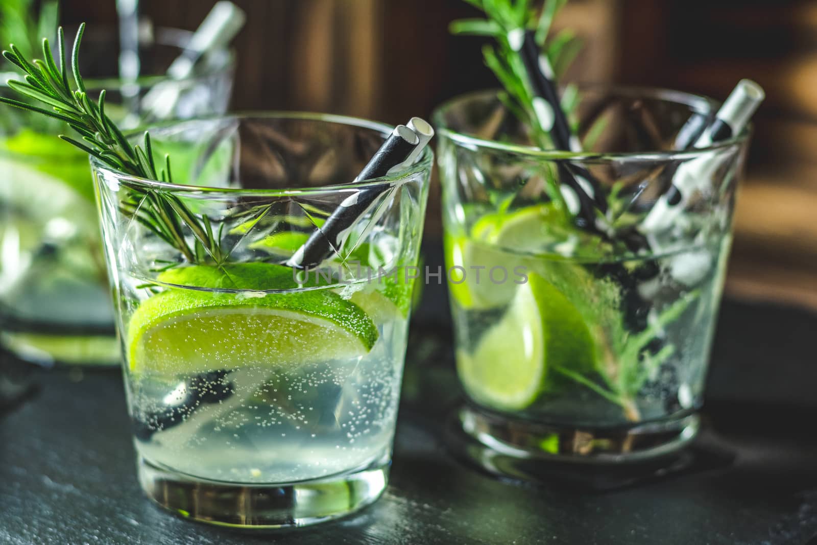 Fresh cocktail with lime, ice and rosemary, mojito cocktail in a bur on a rustic table, selective focus, shallow depth of the field.