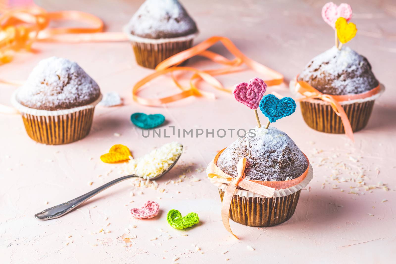 Tasty delicious homemade muffin on light pink living coral stone concrete surface with knitting hearts, copy space. Sweet food for valentines day.