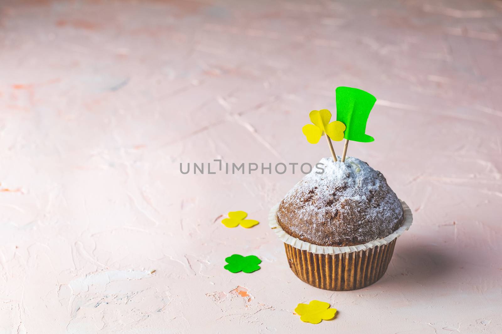 Tasty delicious homemade muffins on light pink living coral stone concrete surface with holiday attributes, copy space. Beautiful sweet food concept for Saint Patrick day.