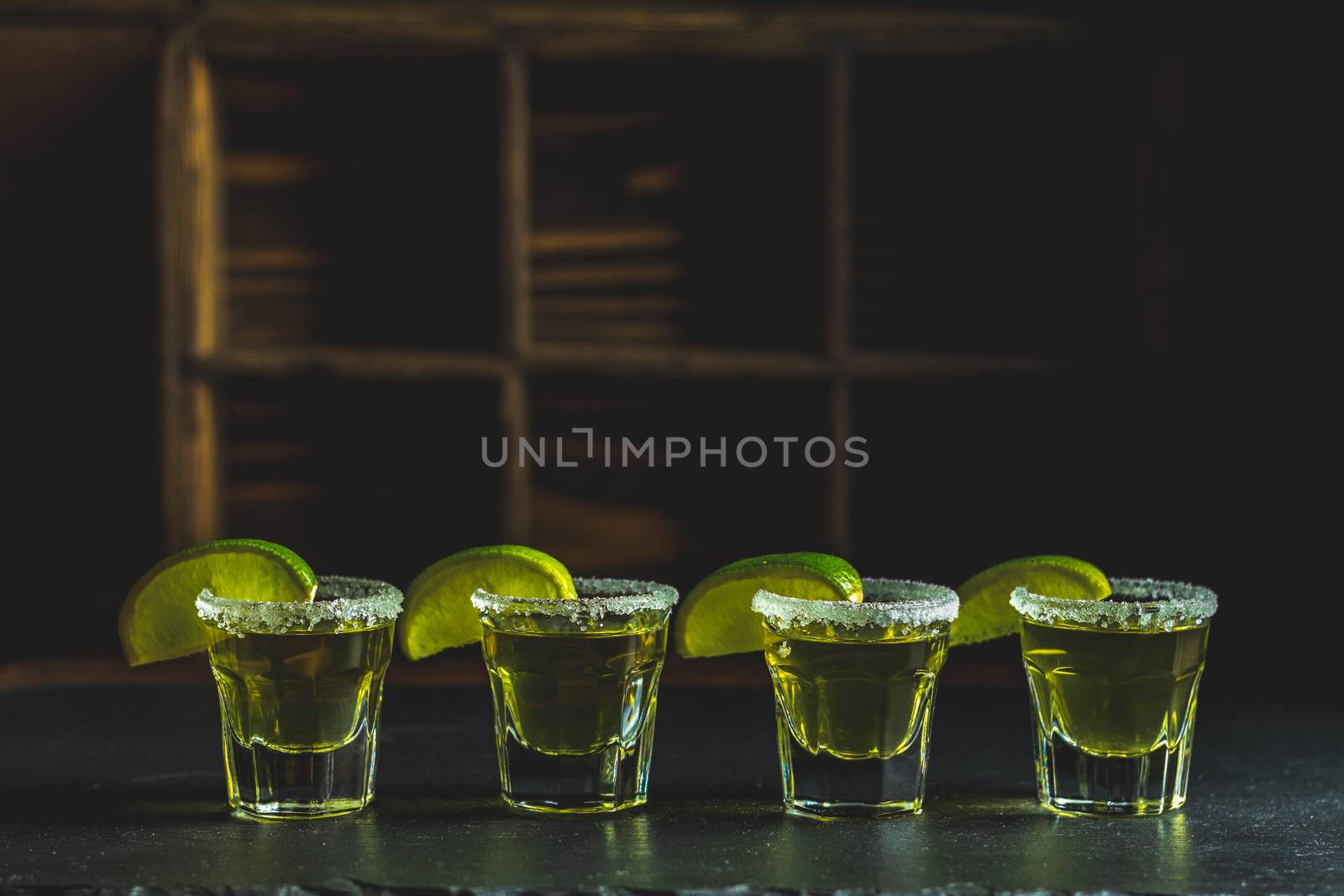 Mexican Gold Tequila shot with lime and salt on black stone table surface, selective focus, shallow depth of the field, copy space.