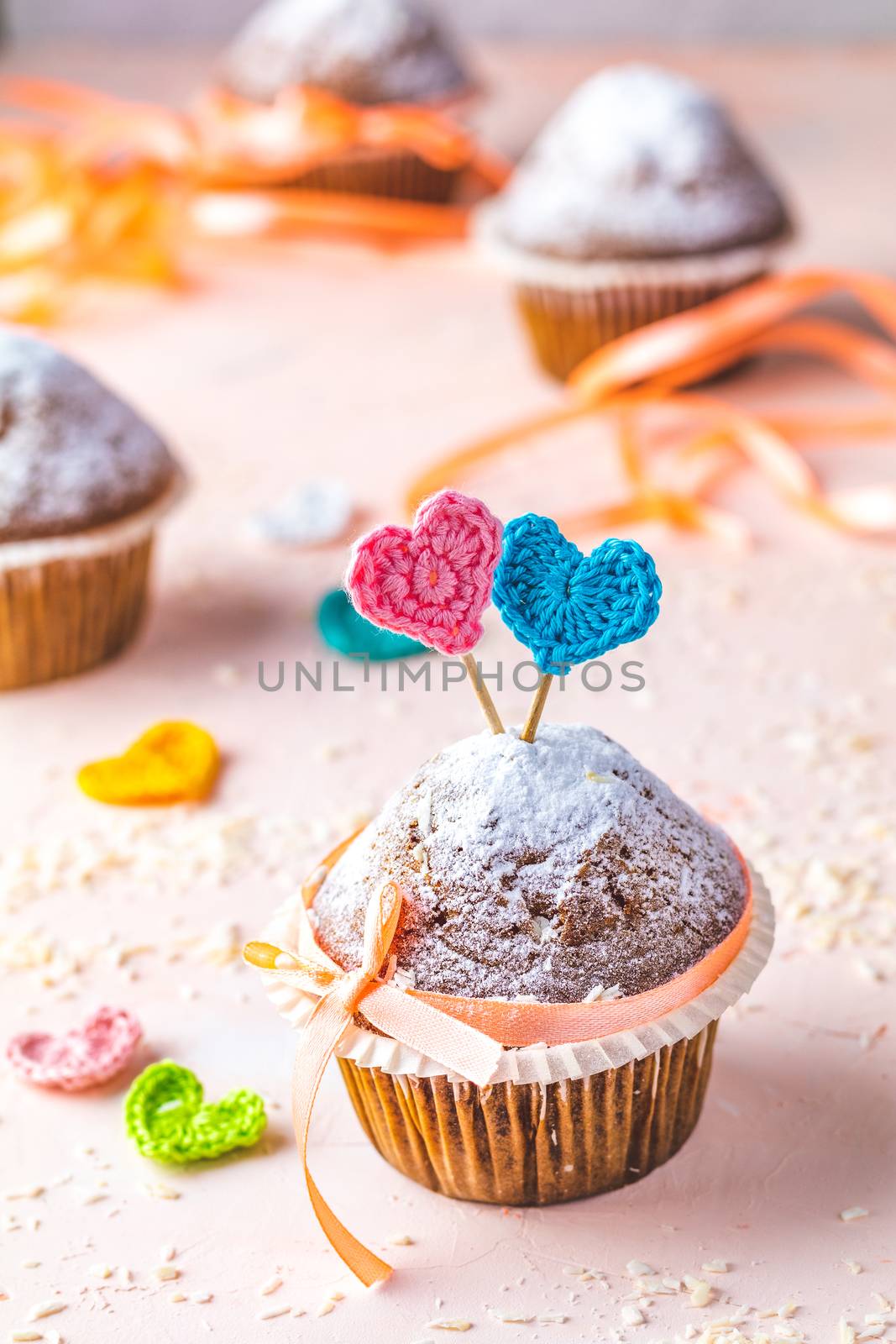 Tasty delicious homemade muffin on light pink living coral stone concrete surface with knitting hearts, copy space. Sweet food for valentines day.