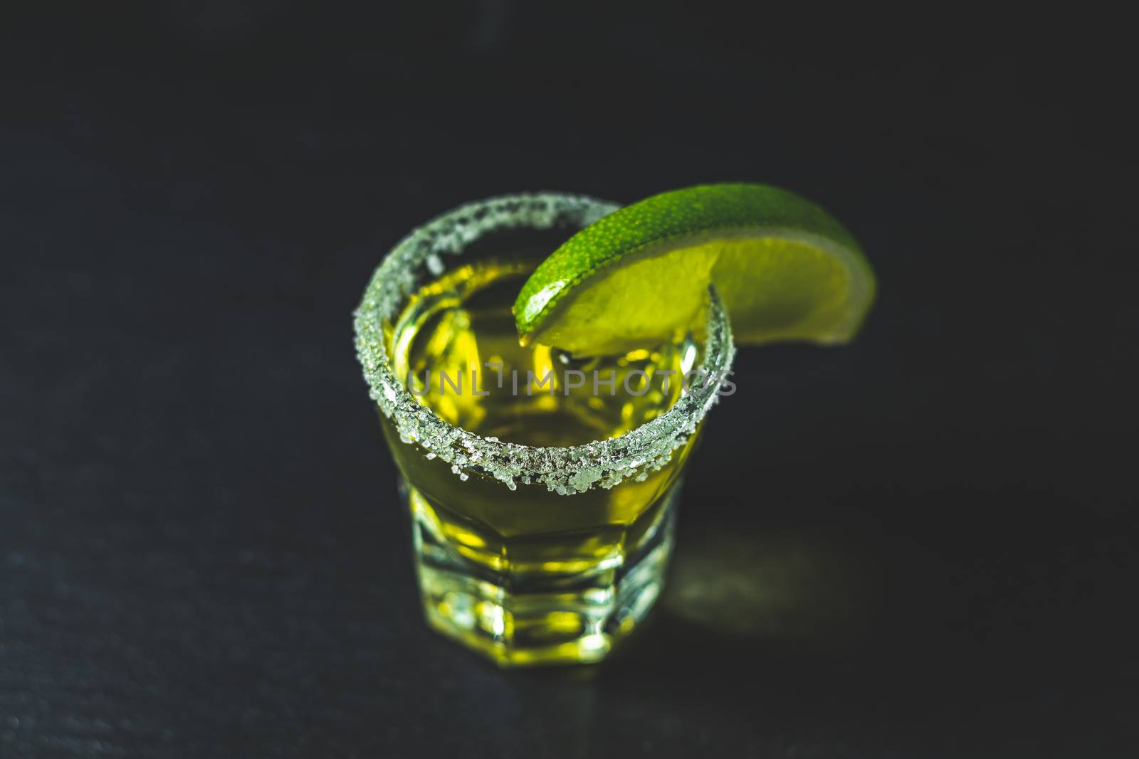 Mexican Gold Tequila shot  with lime and salt on black stone table surface, selective focus, shallow depth of the field, copy space.