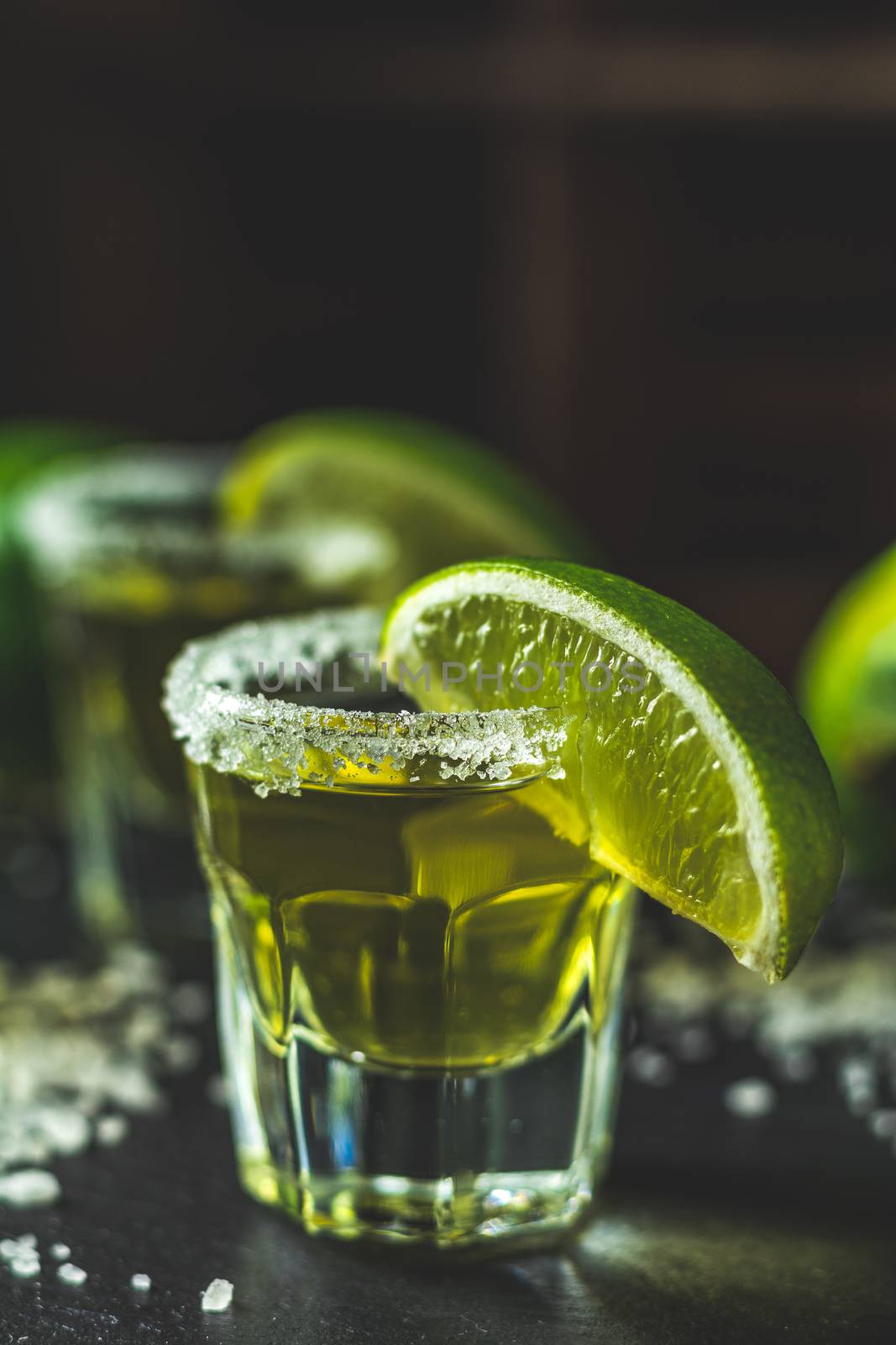 Mexican Gold Tequila shot with lime and salt on black stone table surface, selective focus, shallow depth of the field, copy space.