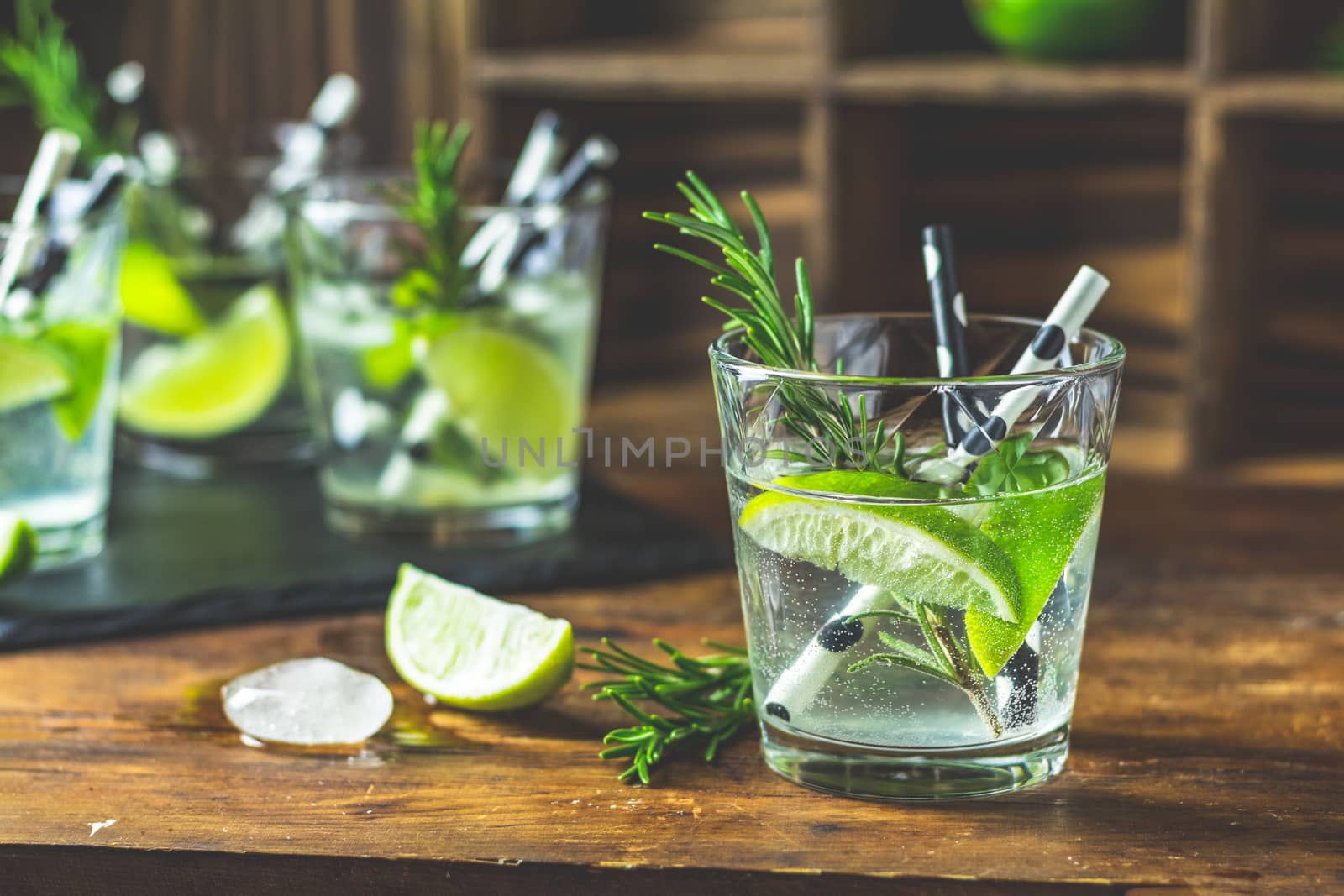 Fresh cocktail with lime, ice and rosemary, mojito cocktail in a bur on a rustic table, selective focus, shallow depth of the field.