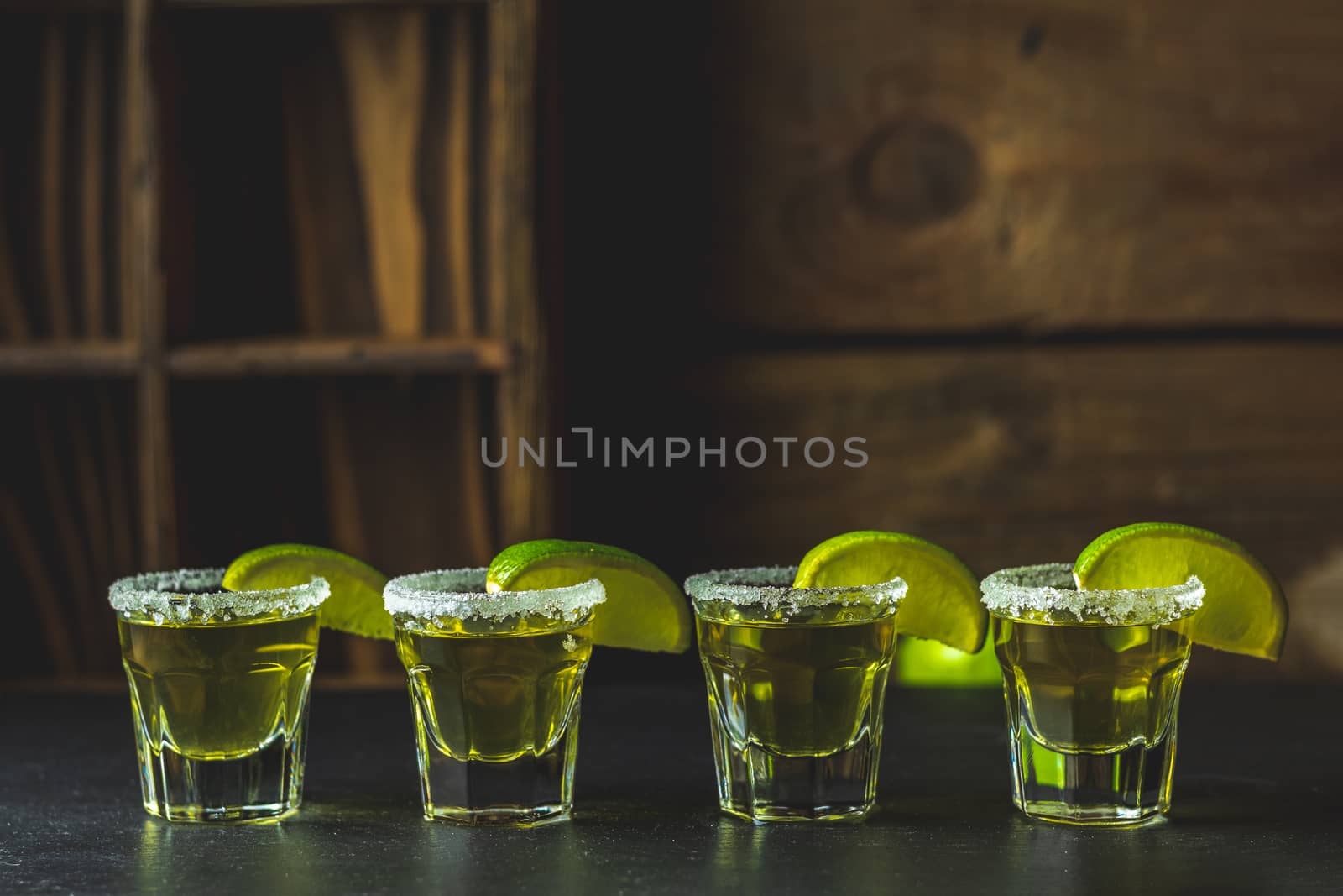 Mexican Gold Tequila shot with lime and salt on black stone table surface, selective focus, shallow depth of the field, copy space.