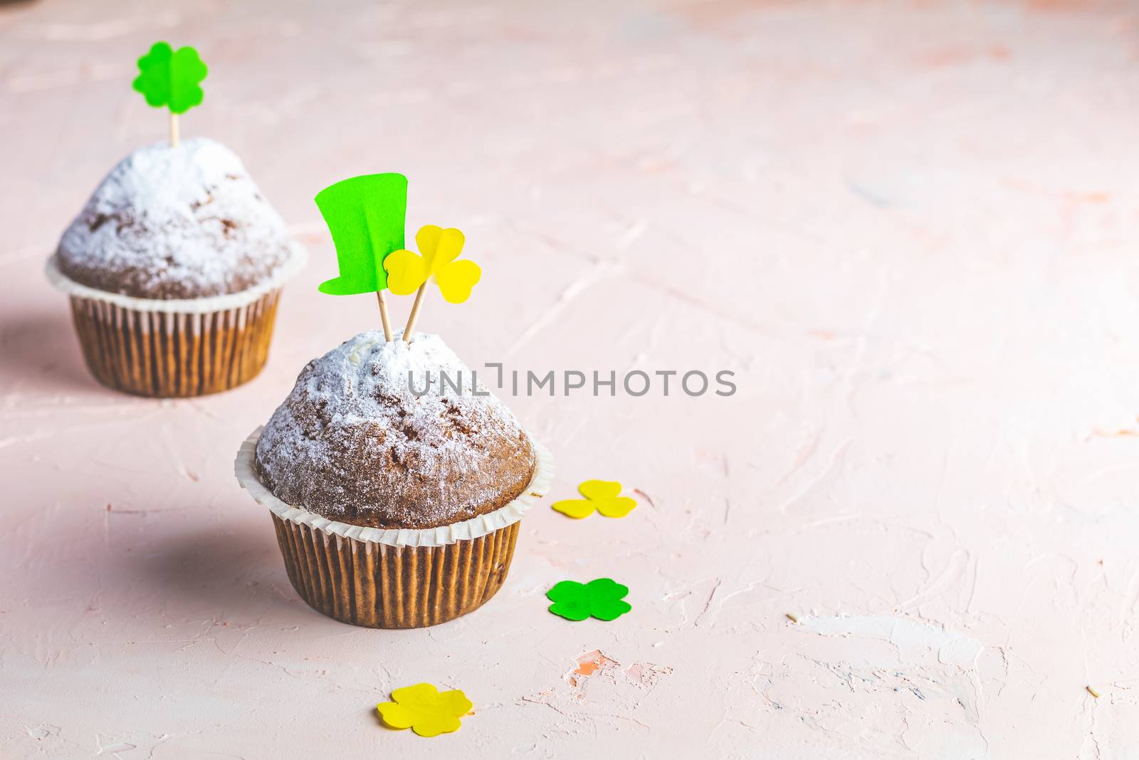 Tasty delicious homemade muffin on light pink living coral stone concrete surface with knitting hearts, copy space. Sweet food for Saint Patrick day.