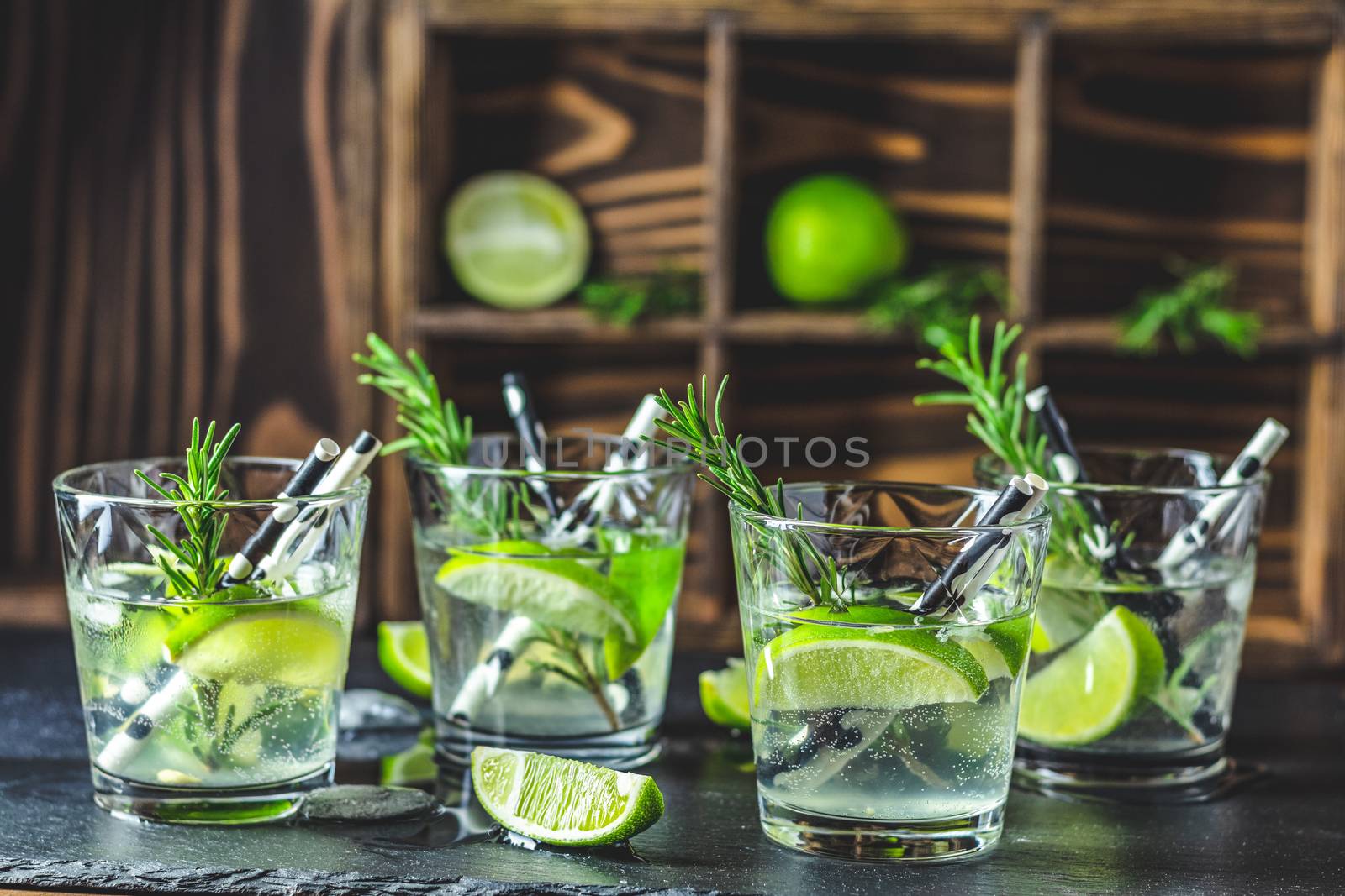 Fresh cocktail with lime, ice and rosemary, mojito cocktail in a bur on a rustic table, selective focus, shallow depth of the field.