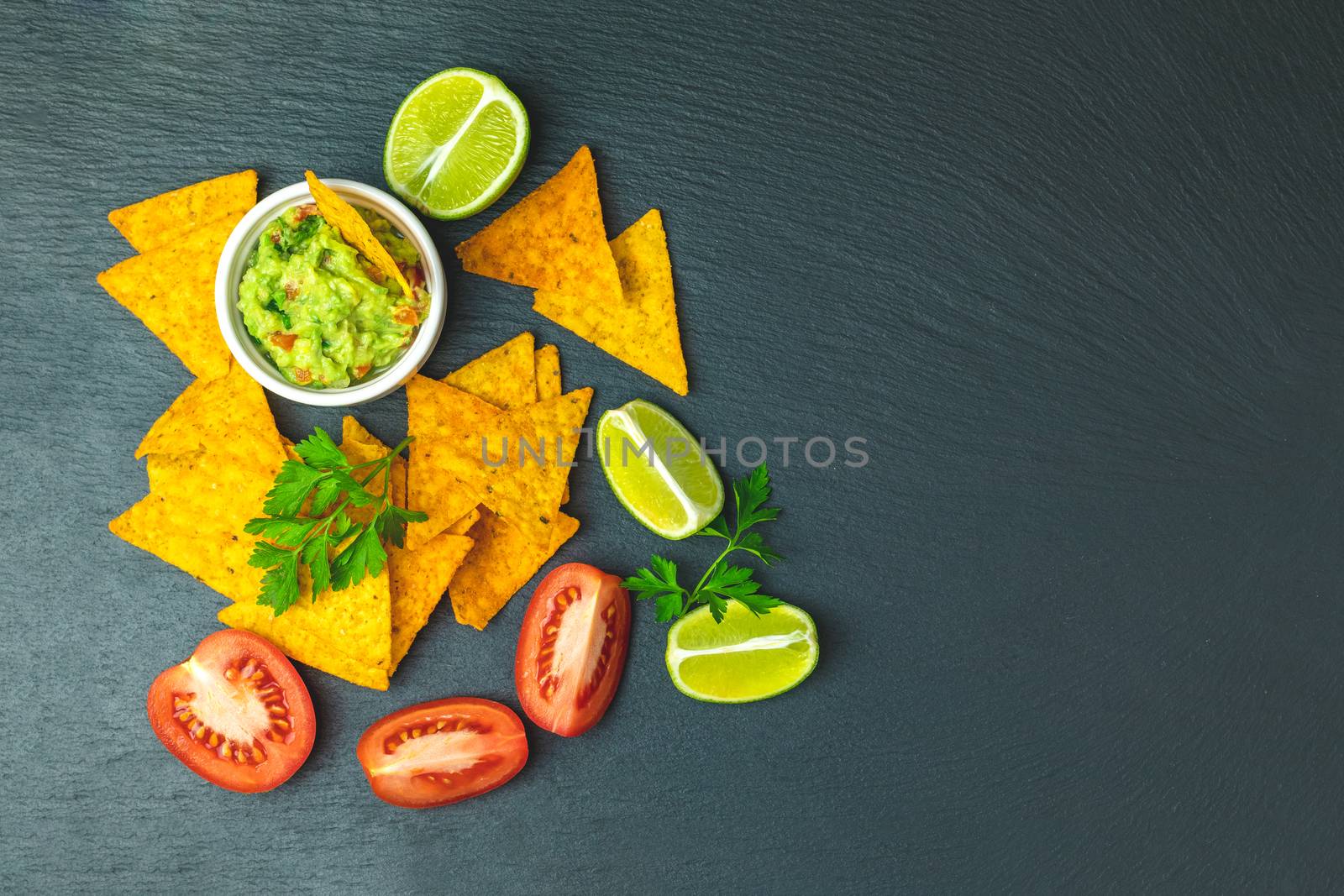 Guacamole and nachos with ingredients on the background of a black stone board. Top view, copy space.