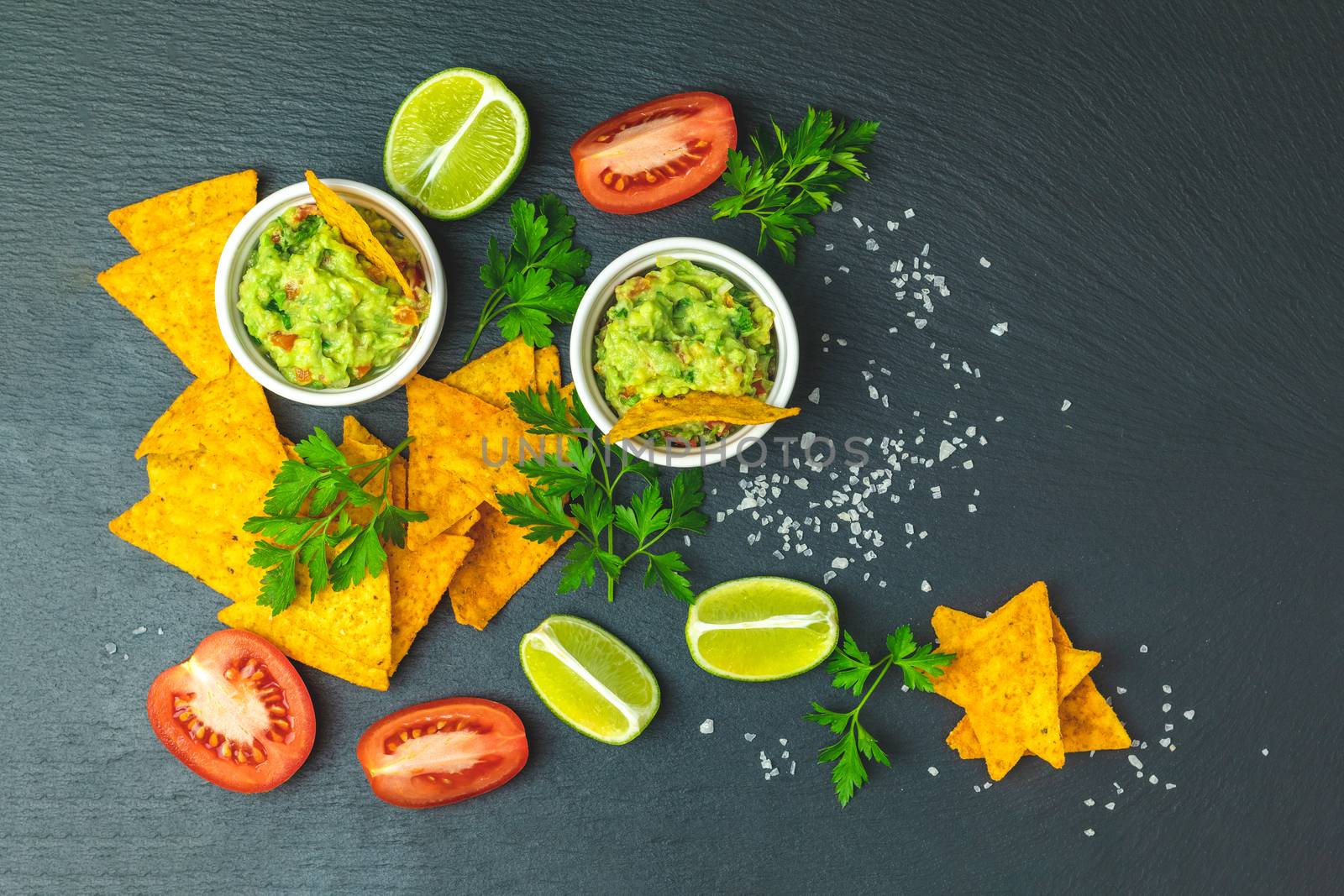 Guacamole and nachos with ingredients on the background of a black stone board. Top view, copy space.