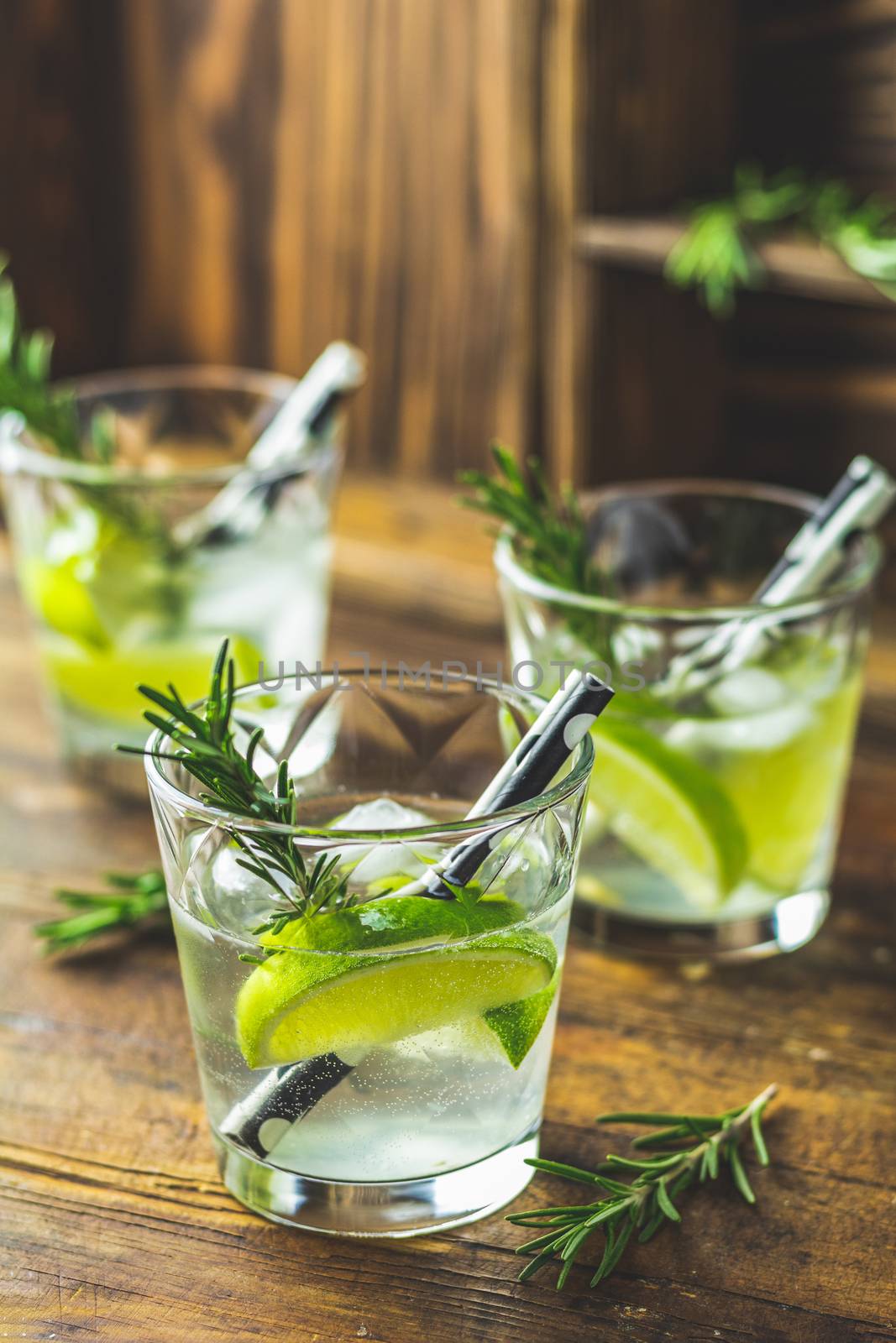 Fresh cocktail with lime, ice and rosemary, mojito cocktail in a bur on a rustic table, selective focus, shallow depth of the field.