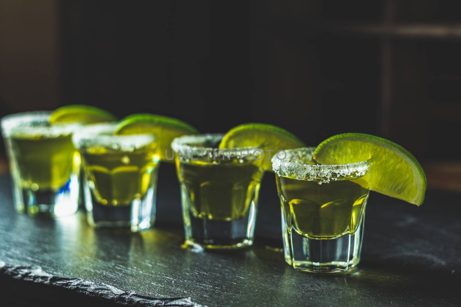 Mexican Gold Tequila shot  with lime and salt on black stone table surface, selective focus, shallow depth of the field, copy space.