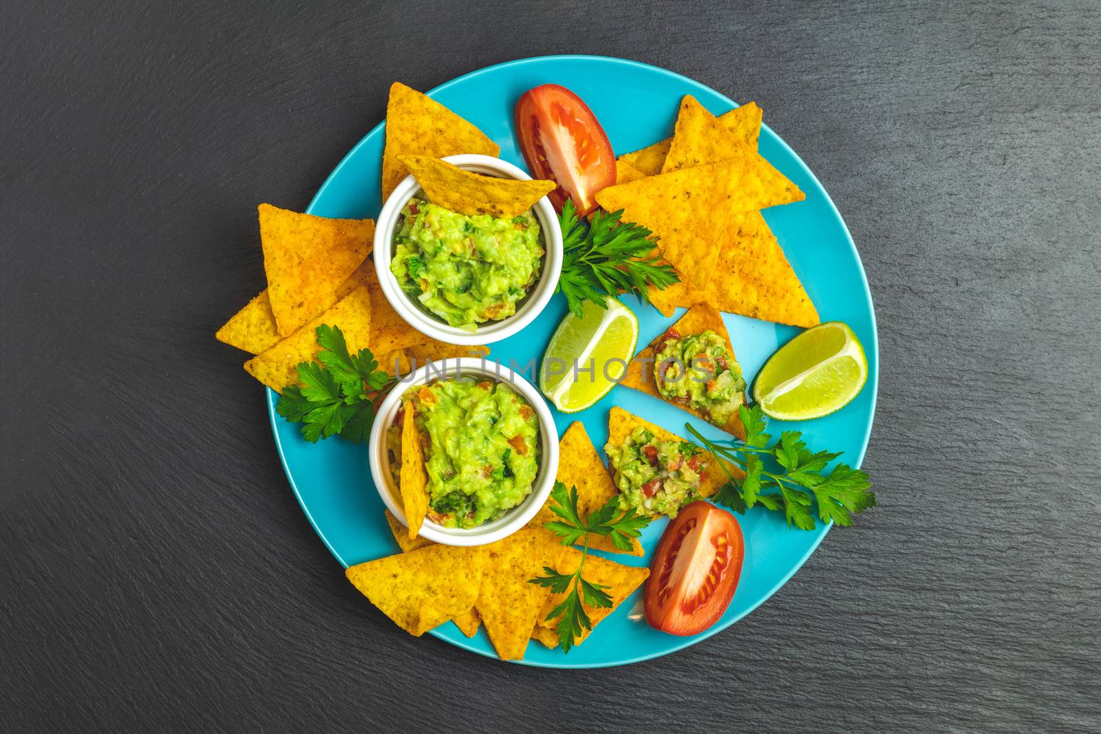 Guacamole and nachos with ingredients in the blue plate on the background of a black stone board. Top view, copy space.