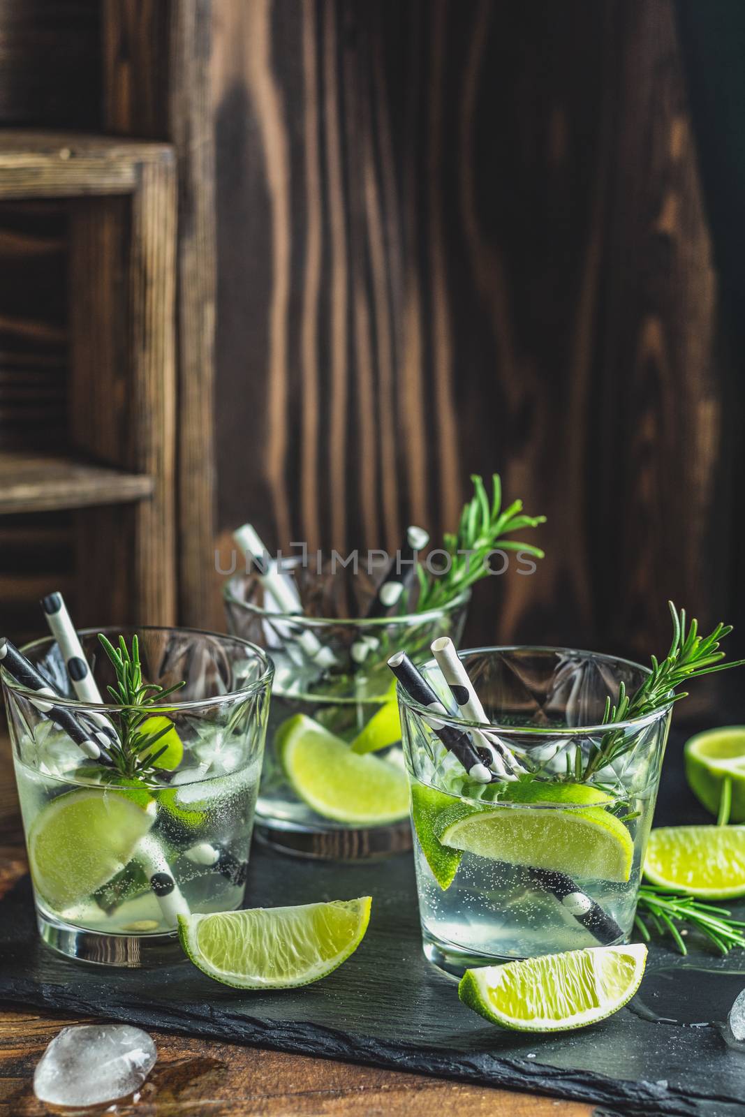 Fresh cocktail with lime, ice and rosemary, mojito cocktail in a bur on a rustic table, selective focus, shallow depth of the field.