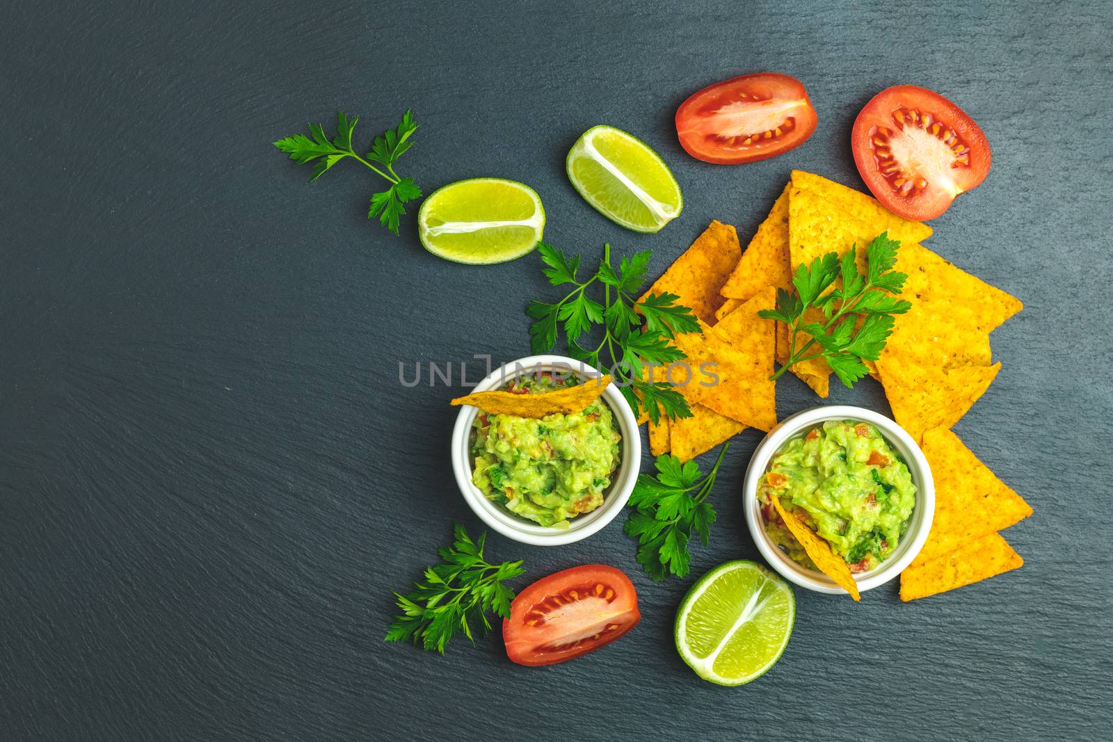 Guacamole and nachos with ingredients on the background of a black stone board. Top view, copy space.