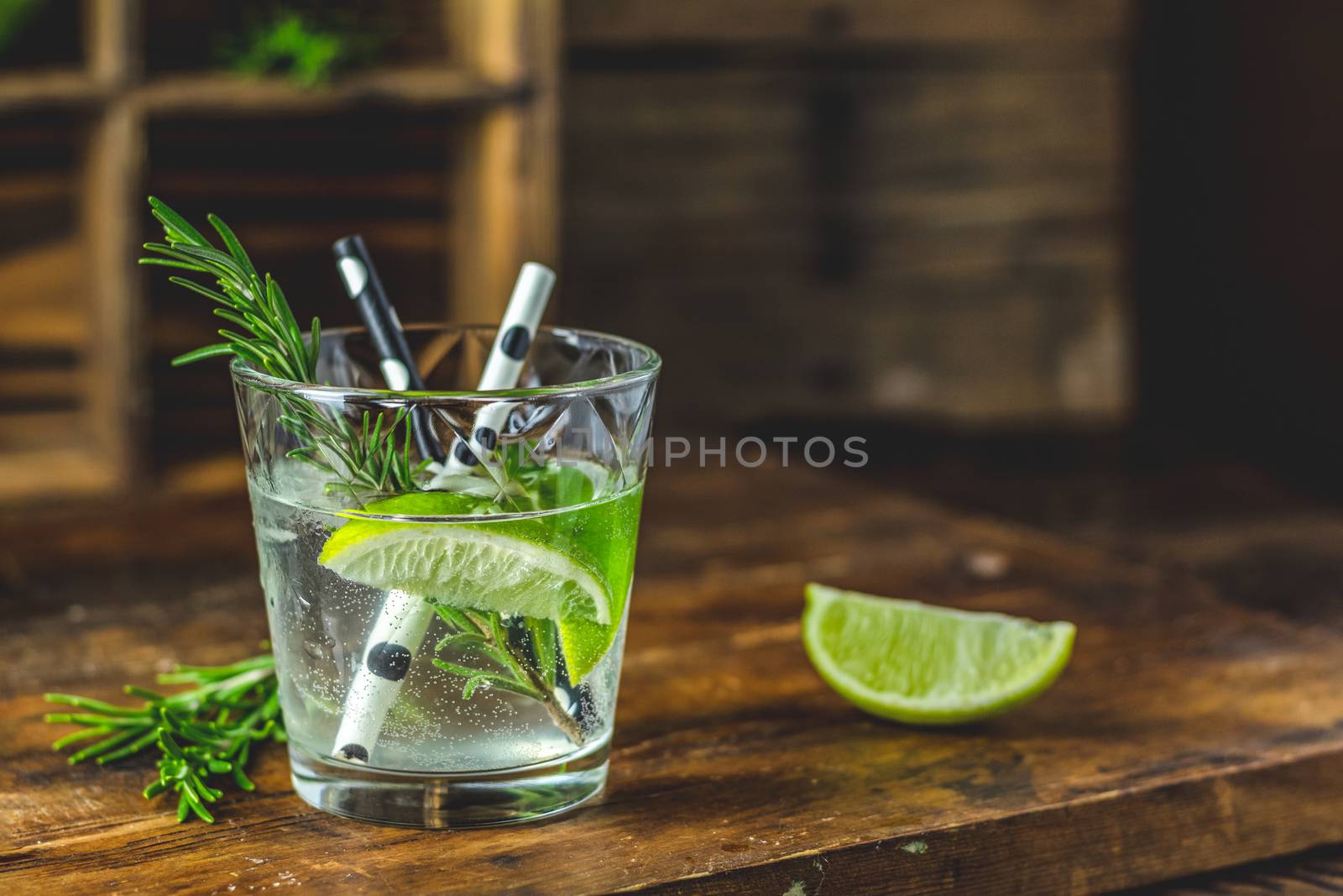 Fresh cocktail with lime, ice and rosemary, mojito cocktail in a bur on a rustic table, selective focus, shallow depth of the field.