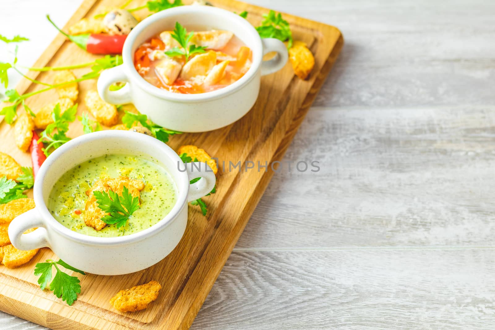 Concept of healthy vegetable and legume soups. Vegetables soup with carrot, eggs and chicken, mushroom cream soup with herbs and crackers and ingredients. Background of a light gray board, copy space