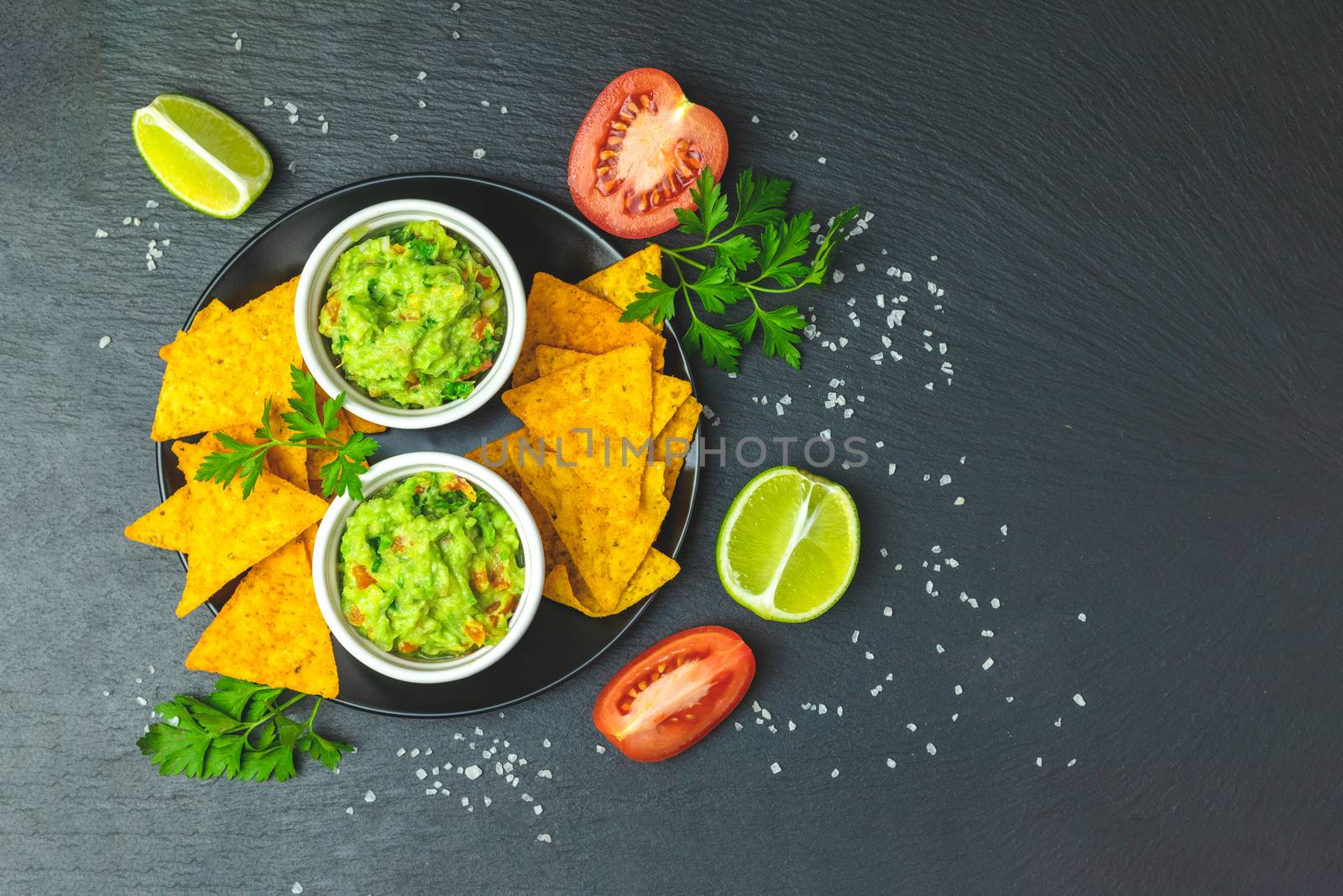 Guacamole and nachos with ingredients on the background of a black stone board. Top view, copy space.