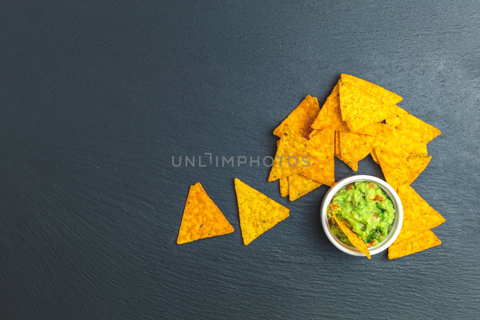 Guacamole and nachos with ingredients on the background of a black stone board. Top view, copy space.