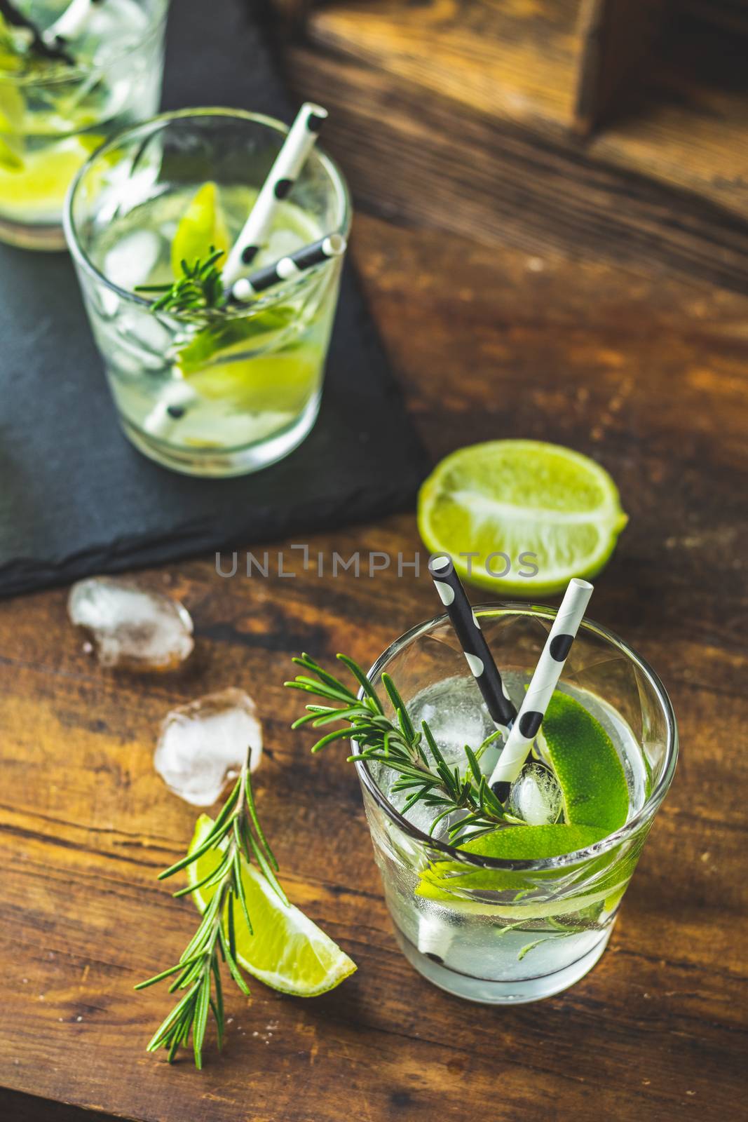 Fresh cocktail with lime, ice and rosemary, mojito cocktail in a bur on a rustic table, selective focus, shallow depth of the field.