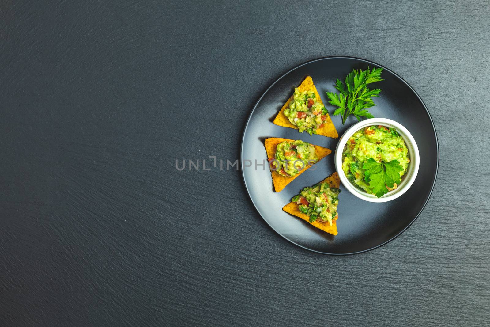 Guacamole and nachos with ingredients on the background of a black stone board. Top view, copy space.