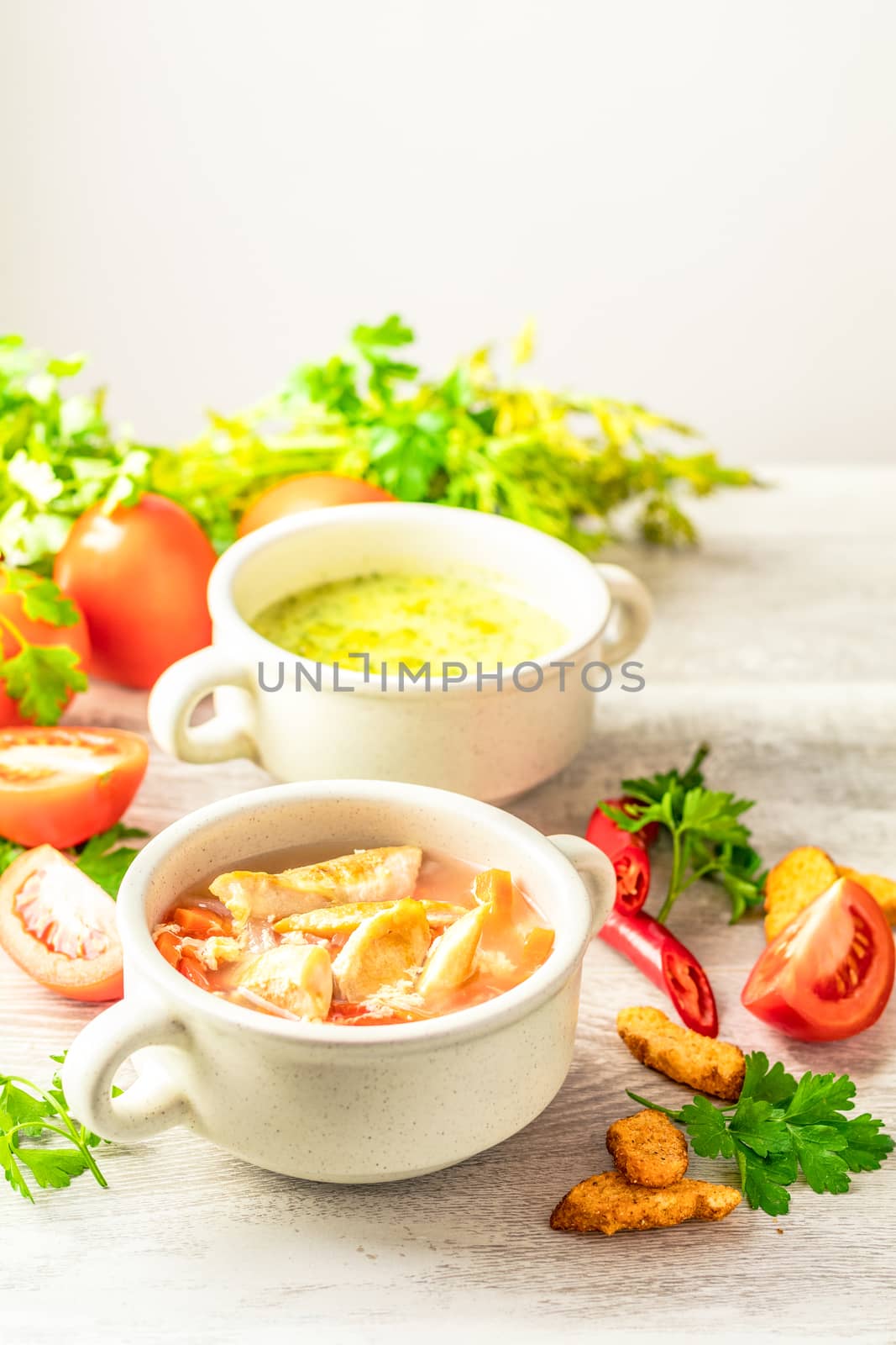 Concept of healthy vegetable and legume soups. Vegetables soup with carrot, eggs and chicken, mushroom cream soup with herbs and crackers and ingredients. Background of a light gray board, copy space