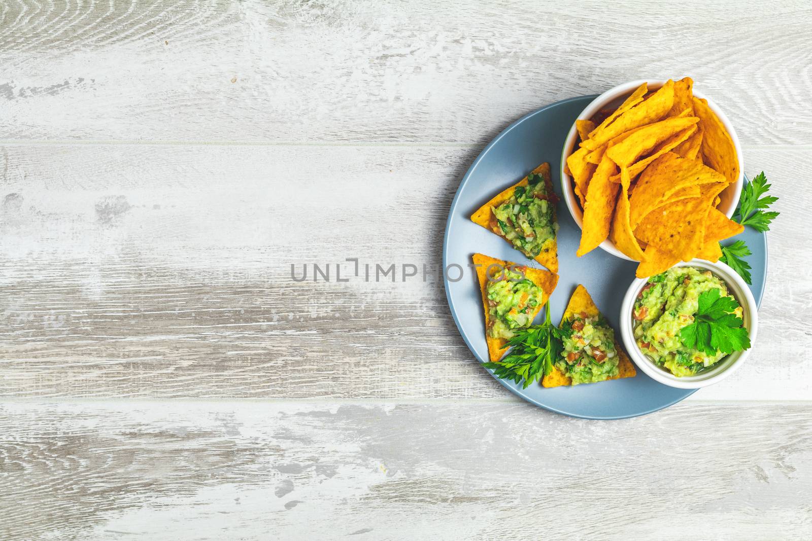 Guacamole and nachos with ingredients on the background of a light gray wooden board. Top view, copy space.