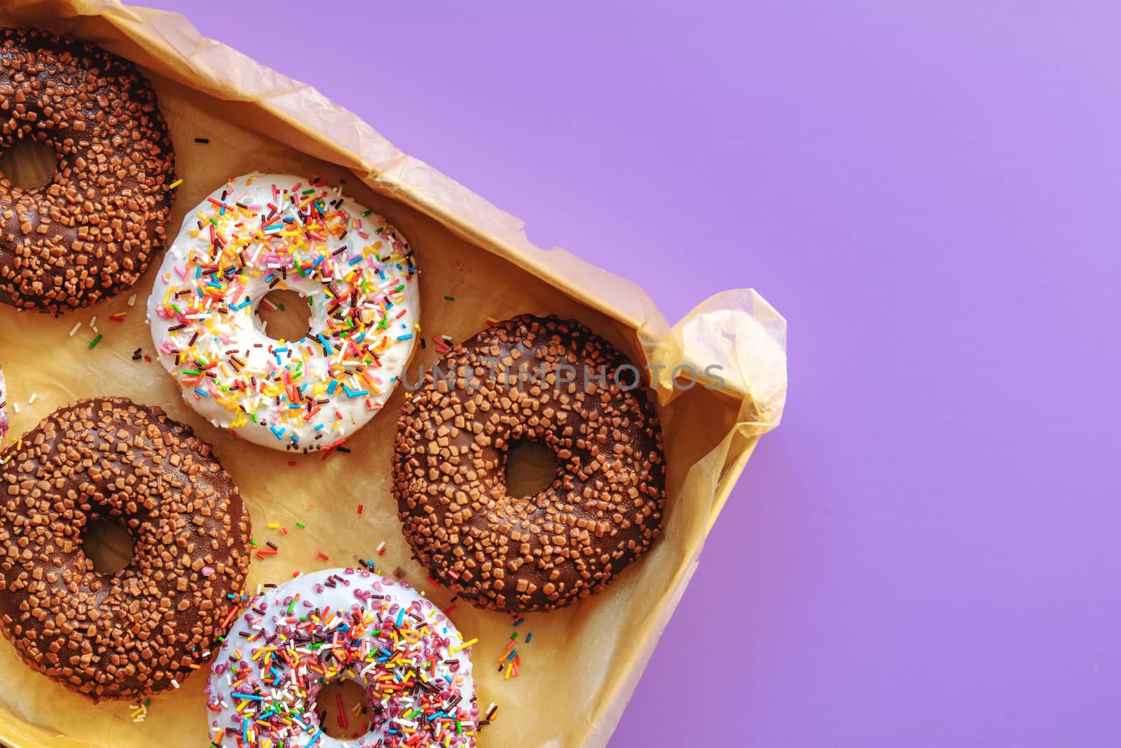 Delicious glazed donuts in box on violet surface. Flat lay minimalist food art background. Top view.