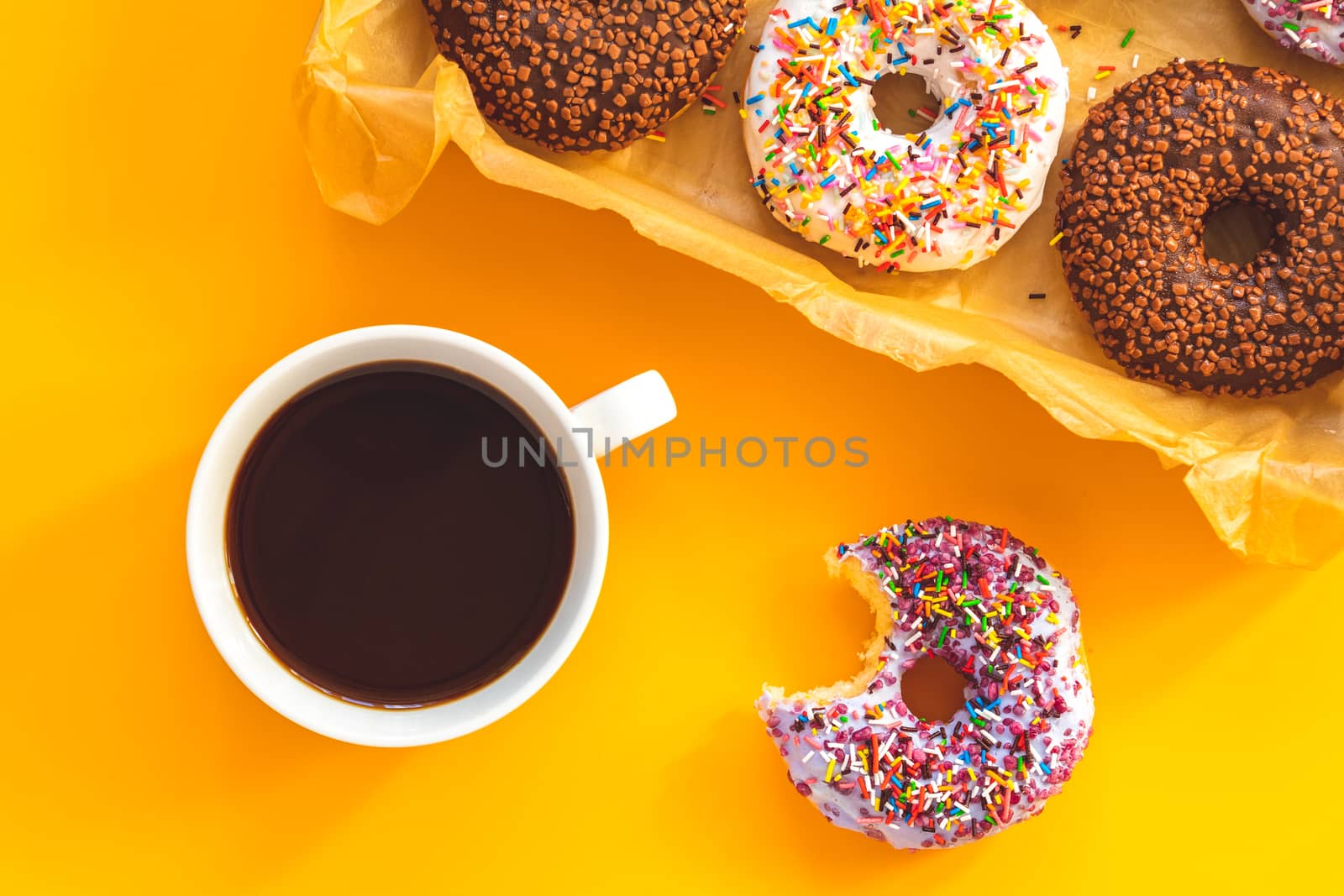Delicious glazed donuts in box and cup of coffee on yellow surfa by ArtSvitlyna