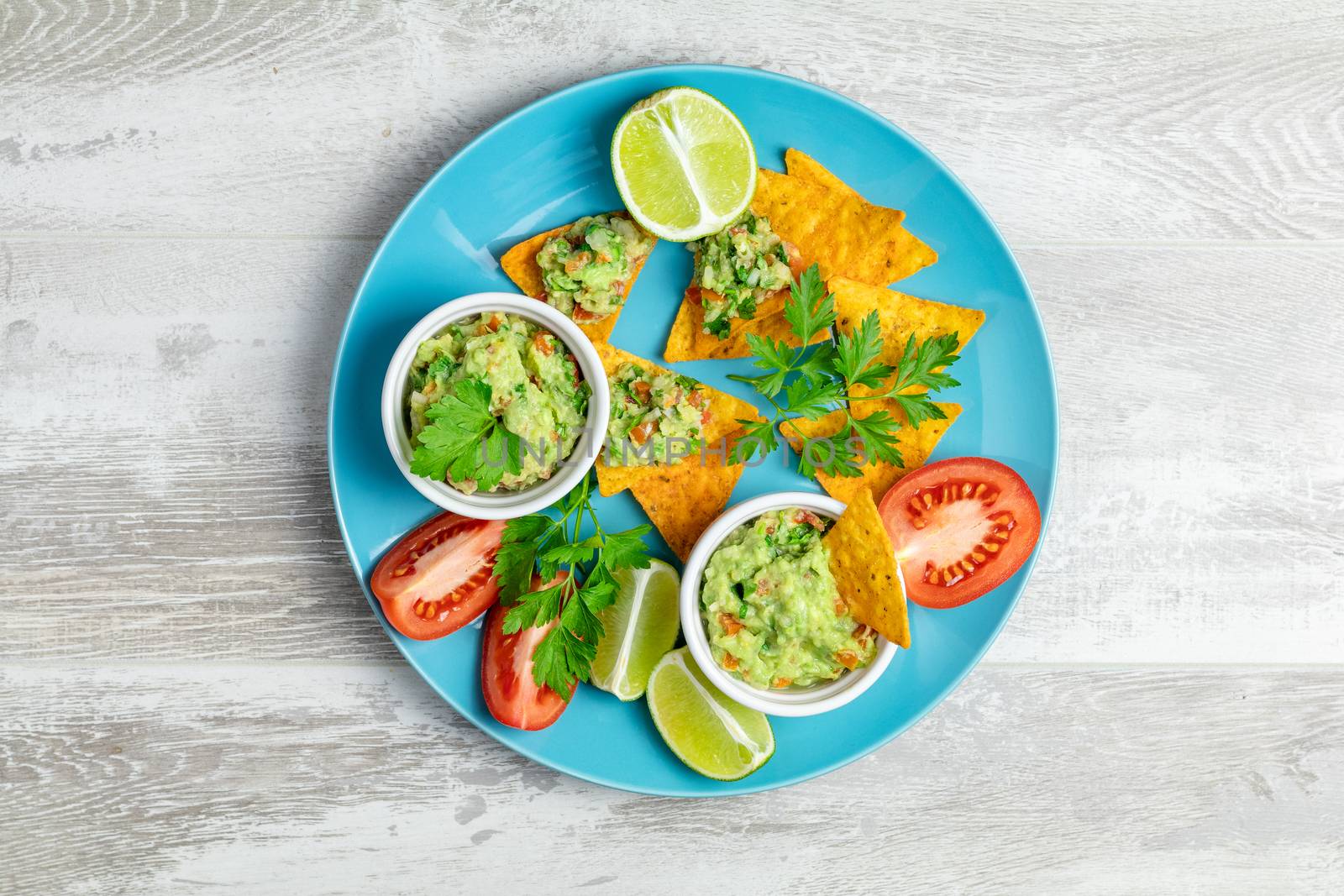 Guacamole and nachos with ingredients on the background of a light gray wooden board. Top view, copy space.