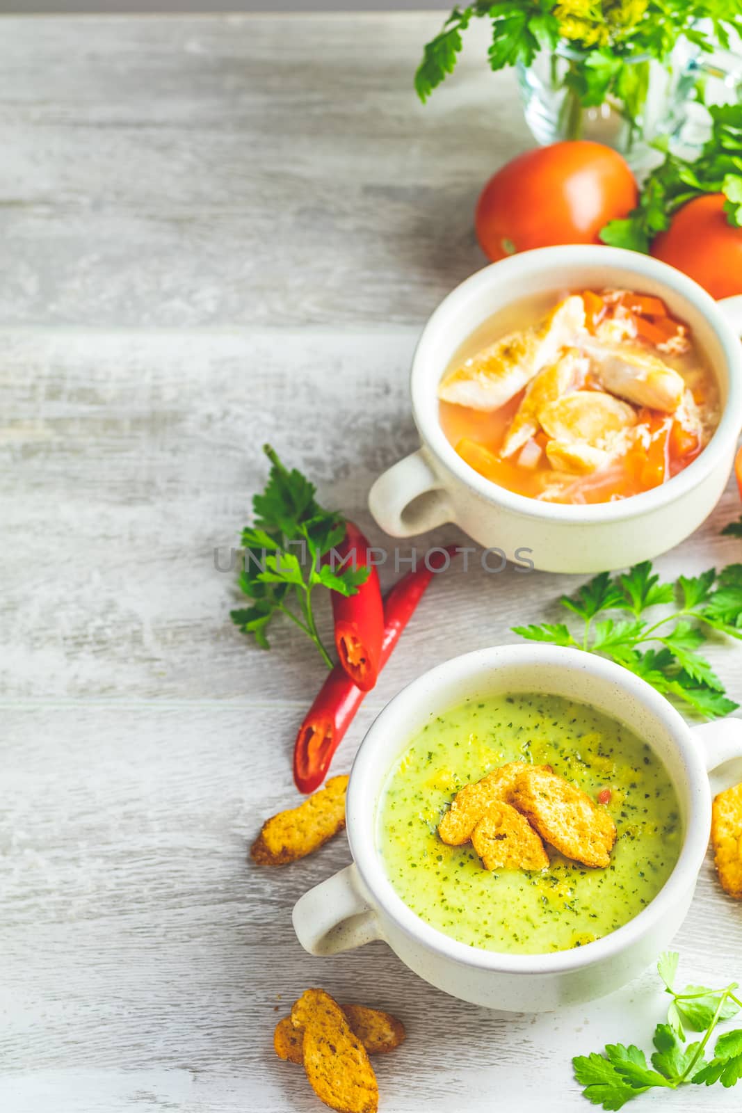 Concept of healthy vegetable and legume soups. Vegetables soup with carrot, eggs and chicken, mushroom cream soup with herbs and crackers and ingredients. Top view on the background of a light gray wooden board, copy space.