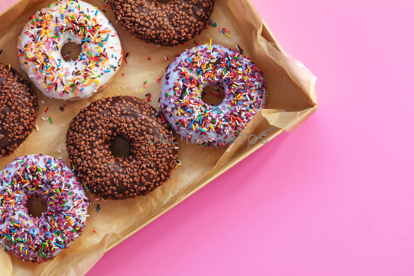 Delicious glazed donuts in box on pink surface. Flat lay minimalist food art background. Top view.
