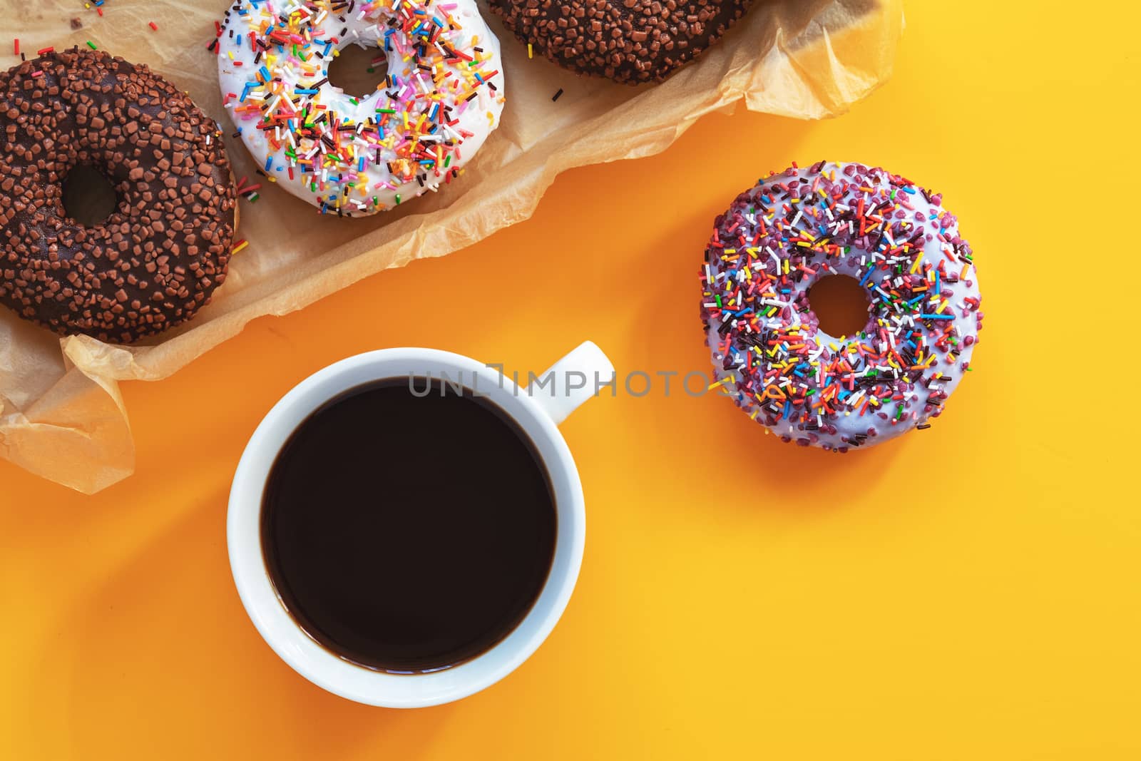 Delicious glazed donuts and cup of coffee on yellow surface by ArtSvitlyna
