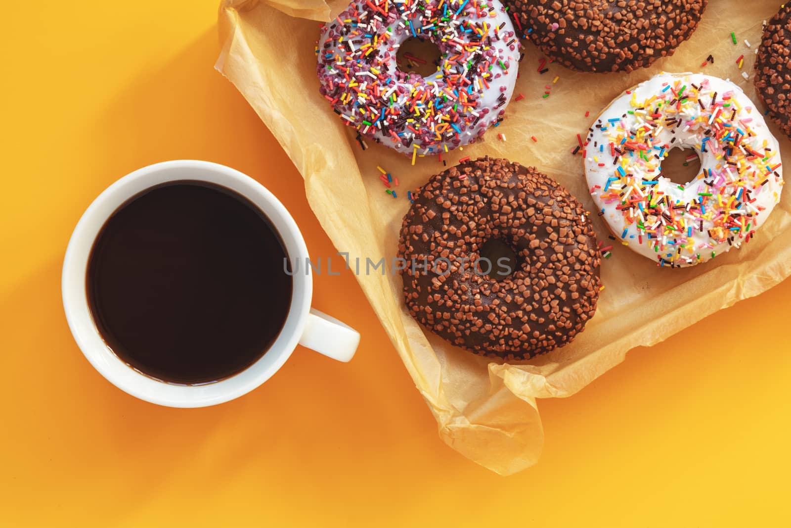 Delicious glazed donuts in box and cup of coffee on yellow surface. Flat lay minimalist food art background. Top view.